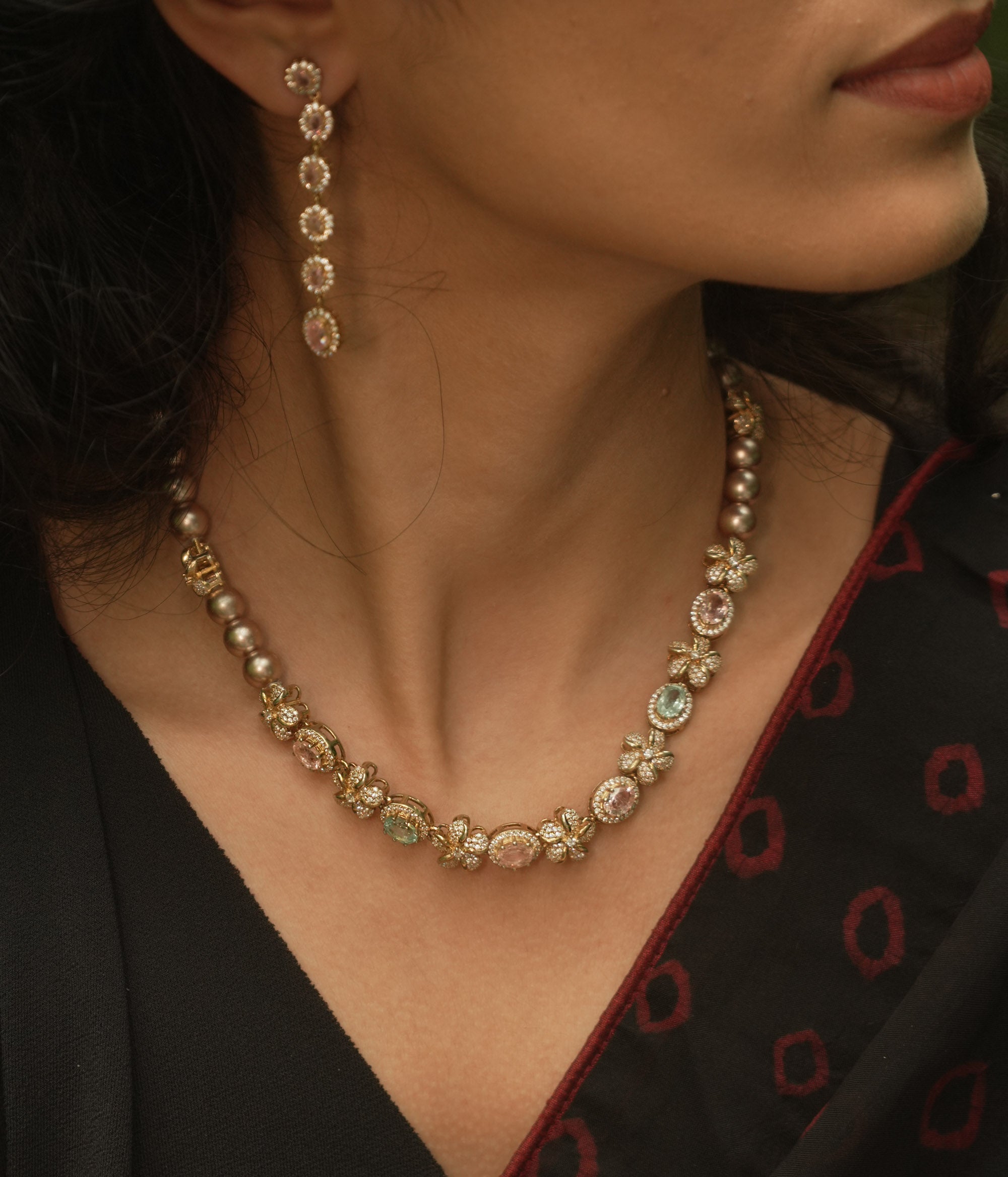 A necklace with multiple strands of pearls and three round, floral medallions with red and green stones.