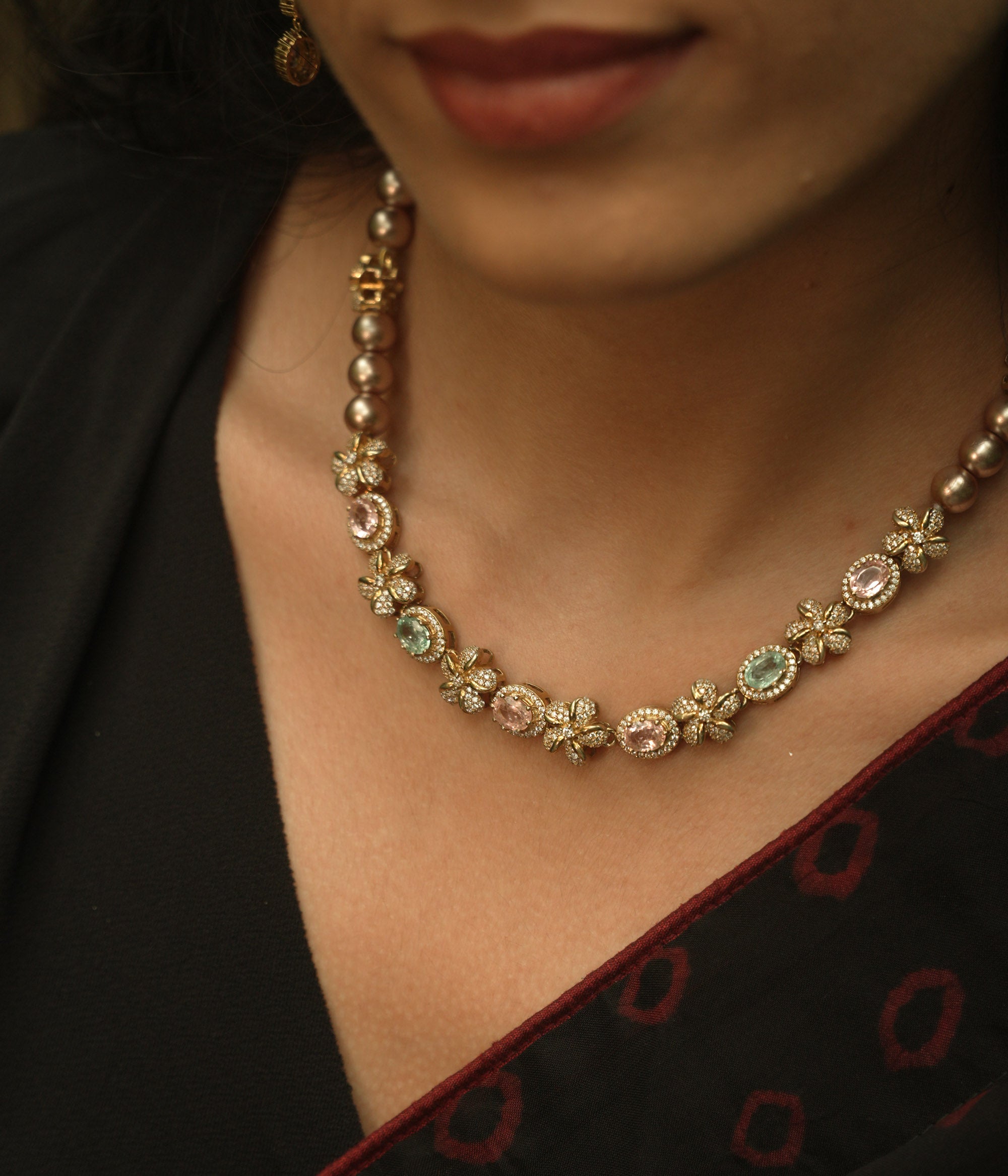 A necklace with multiple strands of pearls and three round, floral medallions with red and green stones.