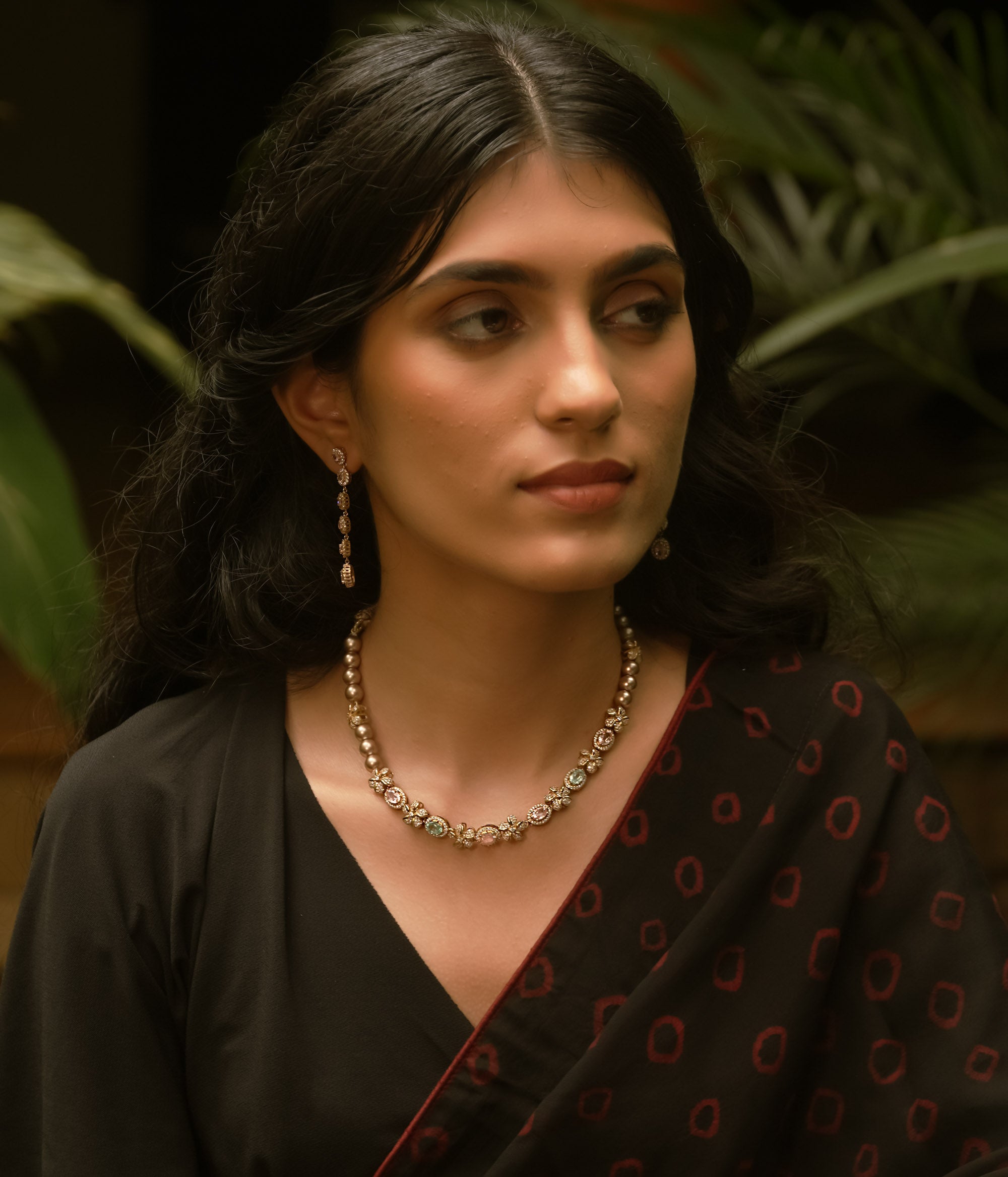 A necklace with multiple strands of pearls and three round, floral medallions with red and green stones.