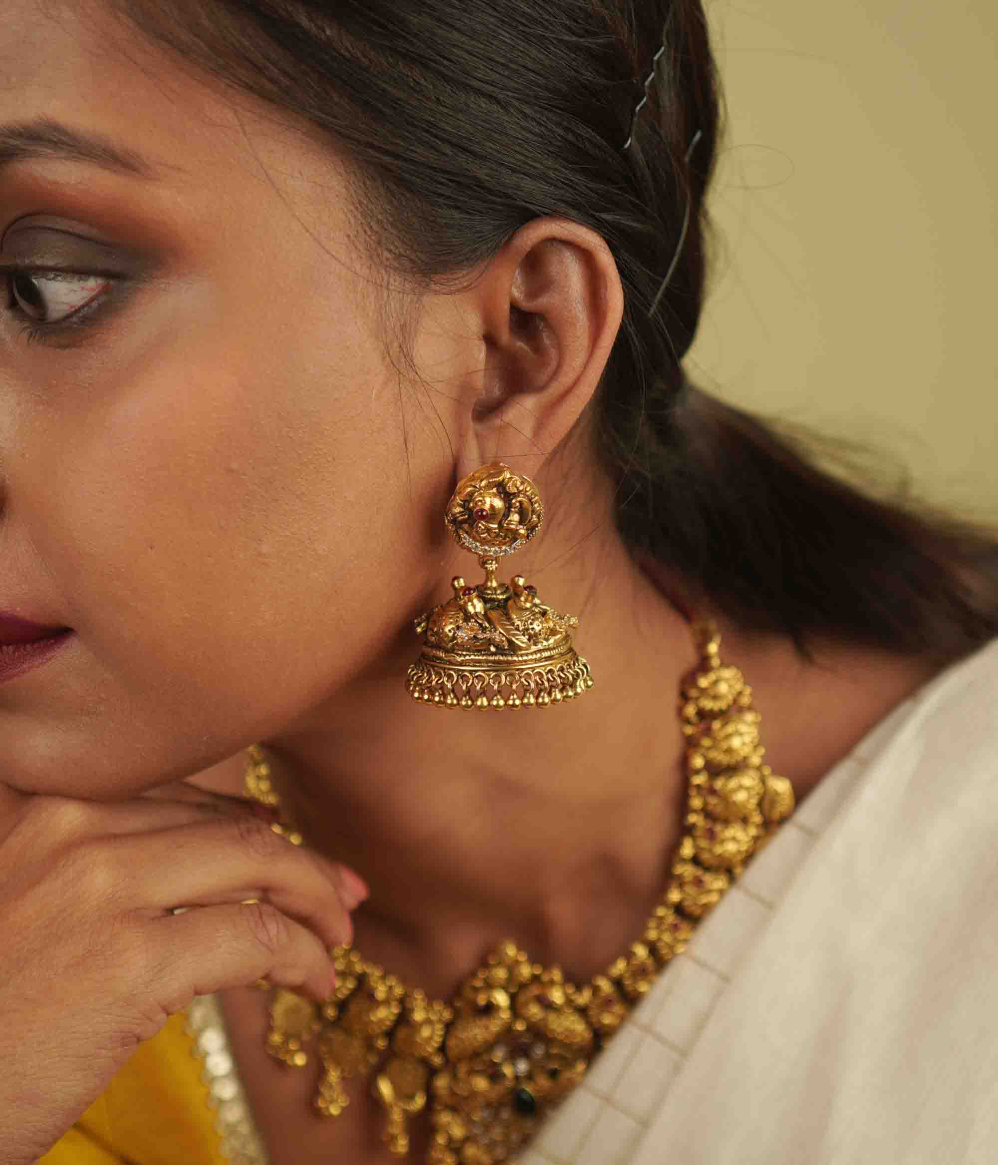 Regal grandeur meets timeless artistry! These gold-plated silver jhumkas, adorned with temple and peacock motifs, shimmer with red spinel and CZ stones, blending heritage craftsmanship with contemporary elegance.