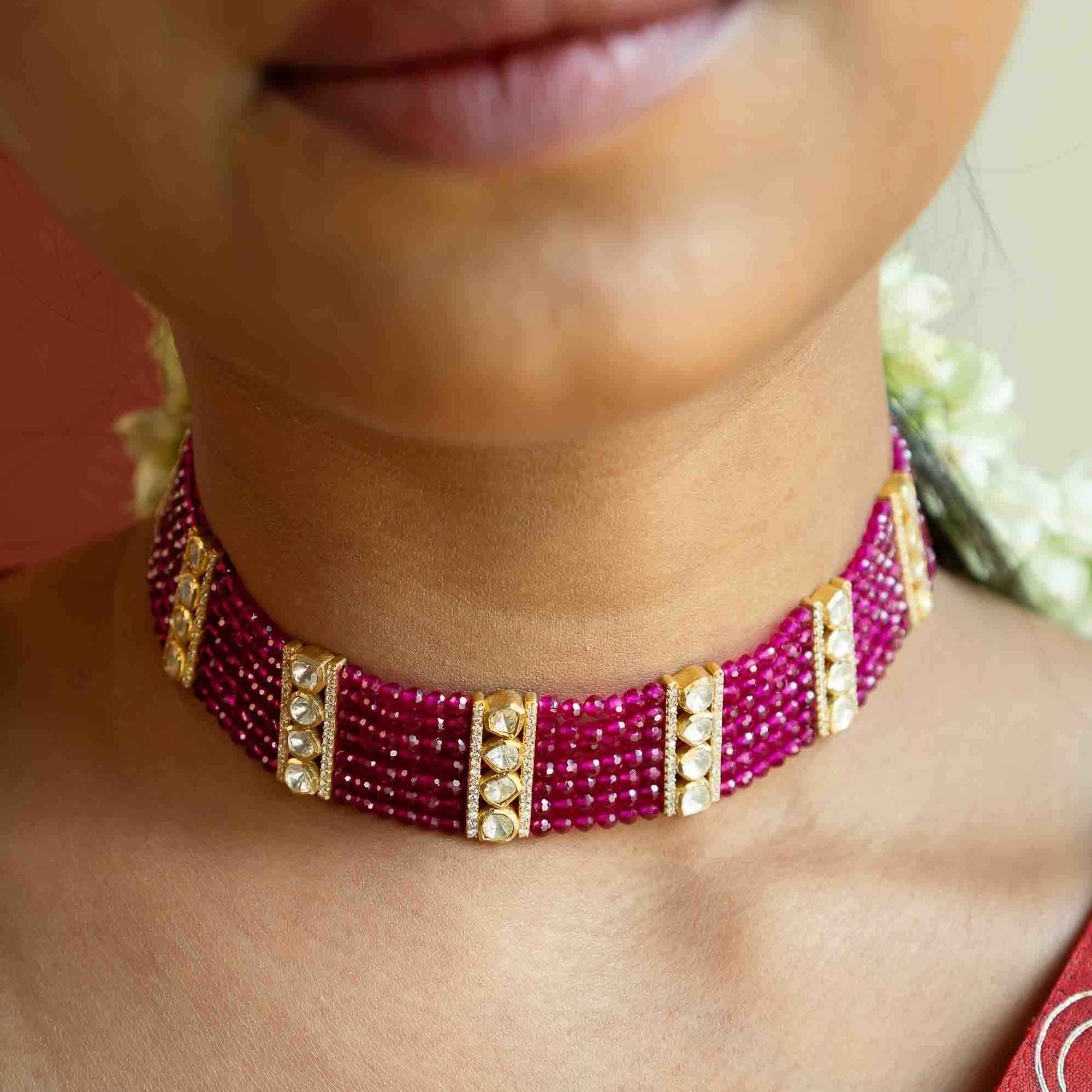 Close-up of a person wearing a pink beaded choker necklace with gold accents.