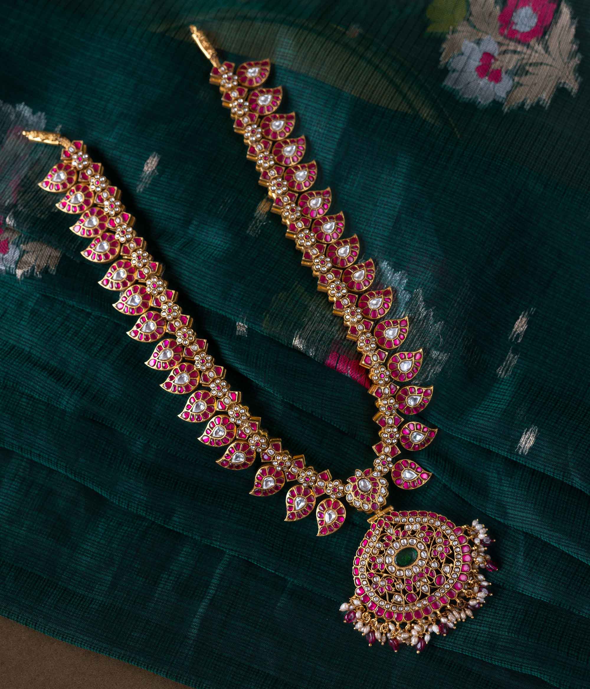 A handcrafted two-sided Kundan necklace in 92.5 sterling silver with 22ct gold plating, adorned with red, white, and green Kundan stones, red beads, and pearls. This versatile masterpiece exudes timeless elegance, blending heritage craftsmanship with regal charm.