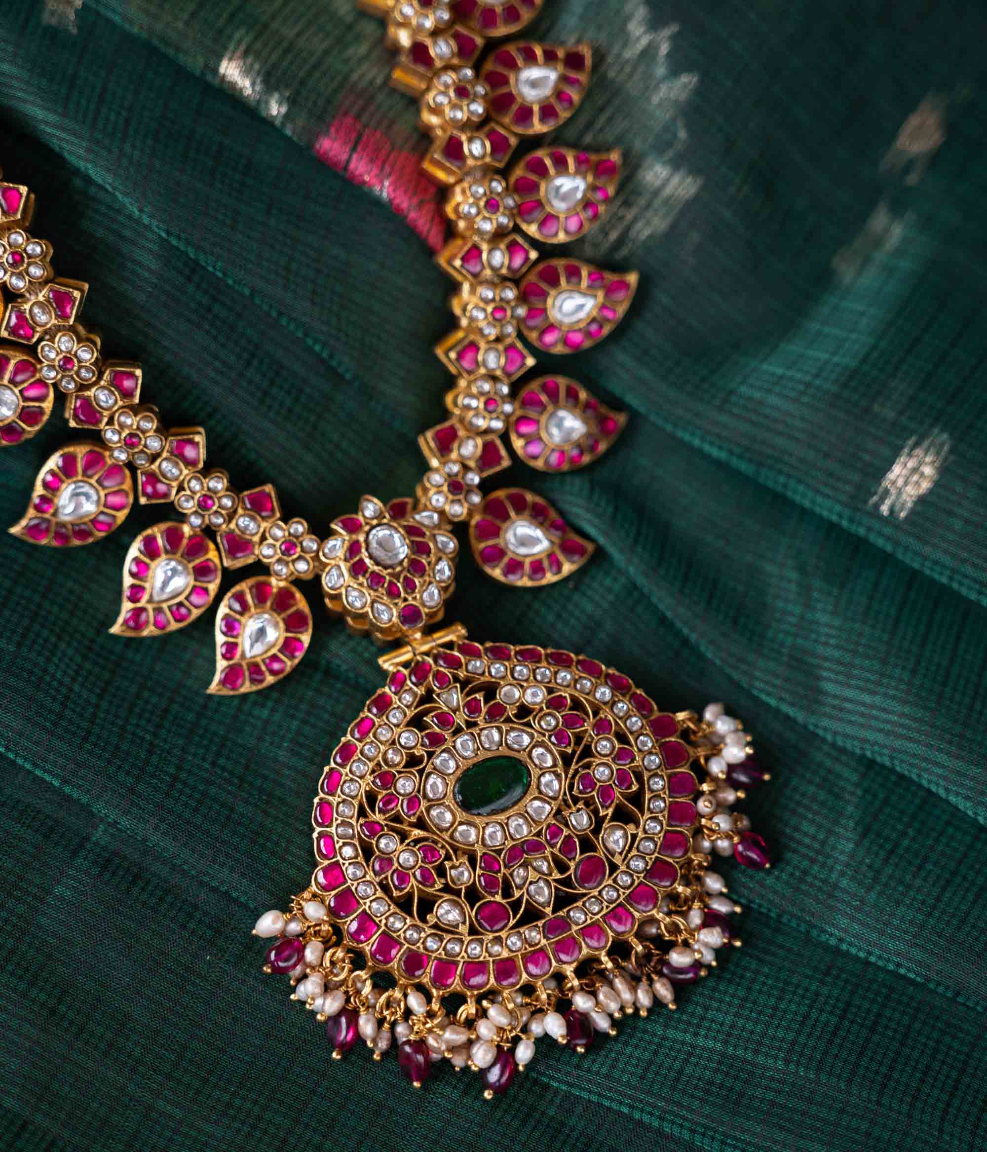 A handcrafted two-sided Kundan necklace in 92.5 sterling silver with 22ct gold plating, adorned with red, white, and green Kundan stones, red beads, and pearls. This versatile masterpiece exudes timeless elegance, blending heritage craftsmanship with regal charm.