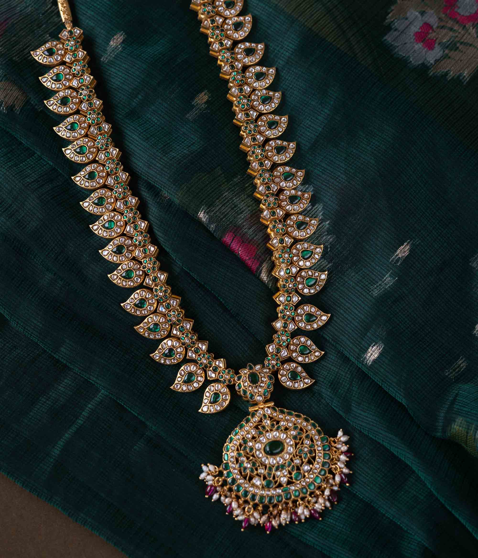 A handcrafted two-sided Kundan necklace in 92.5 sterling silver with 22ct gold plating, adorned with red, white, and green Kundan stones, red beads, and pearls. This versatile masterpiece exudes timeless elegance, blending heritage craftsmanship with regal charm.