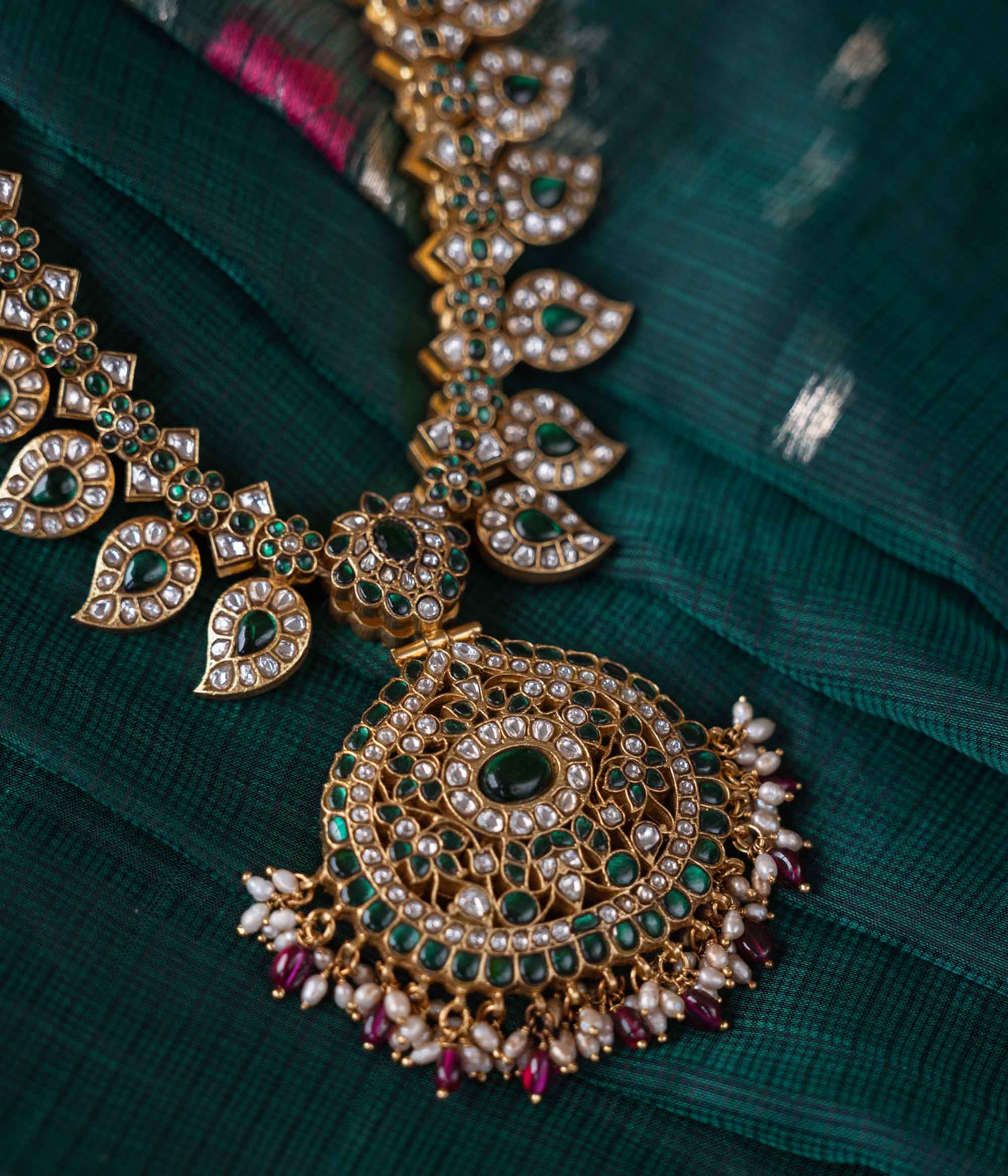 A handcrafted two-sided Kundan necklace in 92.5 sterling silver with 22ct gold plating, adorned with red, white, and green Kundan stones, red beads, and pearls. This versatile masterpiece exudes timeless elegance, blending heritage craftsmanship with regal charm.