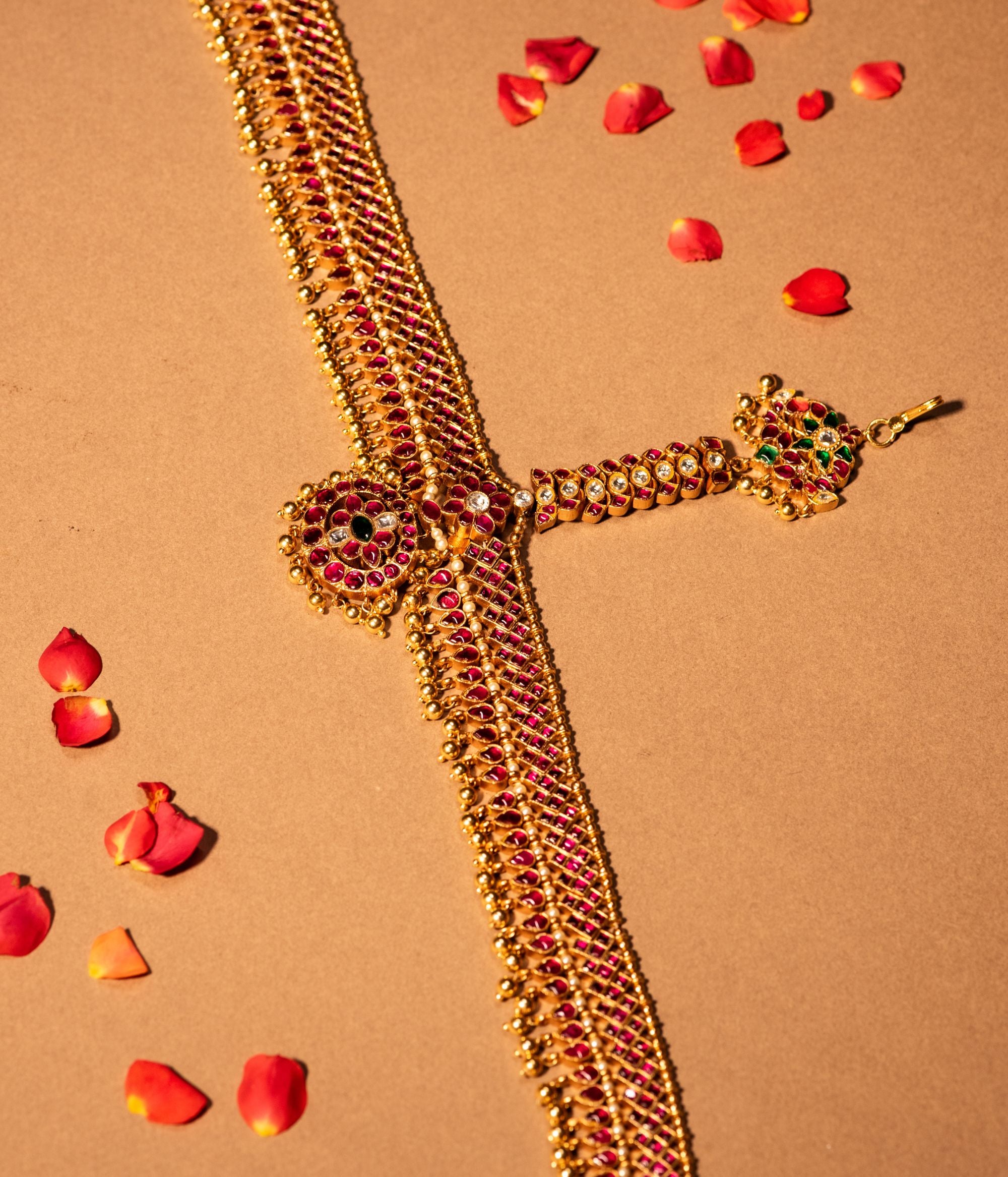 Gold-plated silver tikka with a delicate floral design, adorned with red, green, and white Kundan stones, and finished with golden drop beads, creating a traditional and graceful accessory for Bridal and Festive wear.