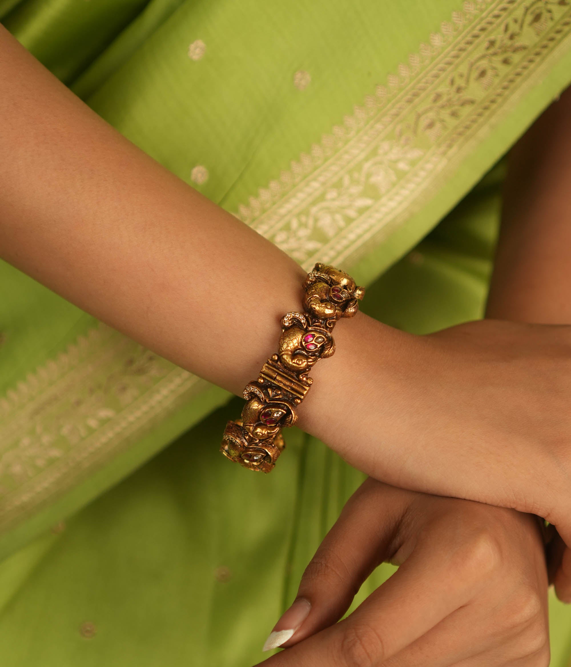 Embrace royal elegance with this stunning antique gold bangle, adorned with vibrant red, white, and green Kundan stones, featuring an intricate peacock motif. The regal peacock comes to life in this piece, while the pink Kundan hues add a touch of grandeur. A perfect fusion of heritage and artistry, this bangle exudes timeless splendor.