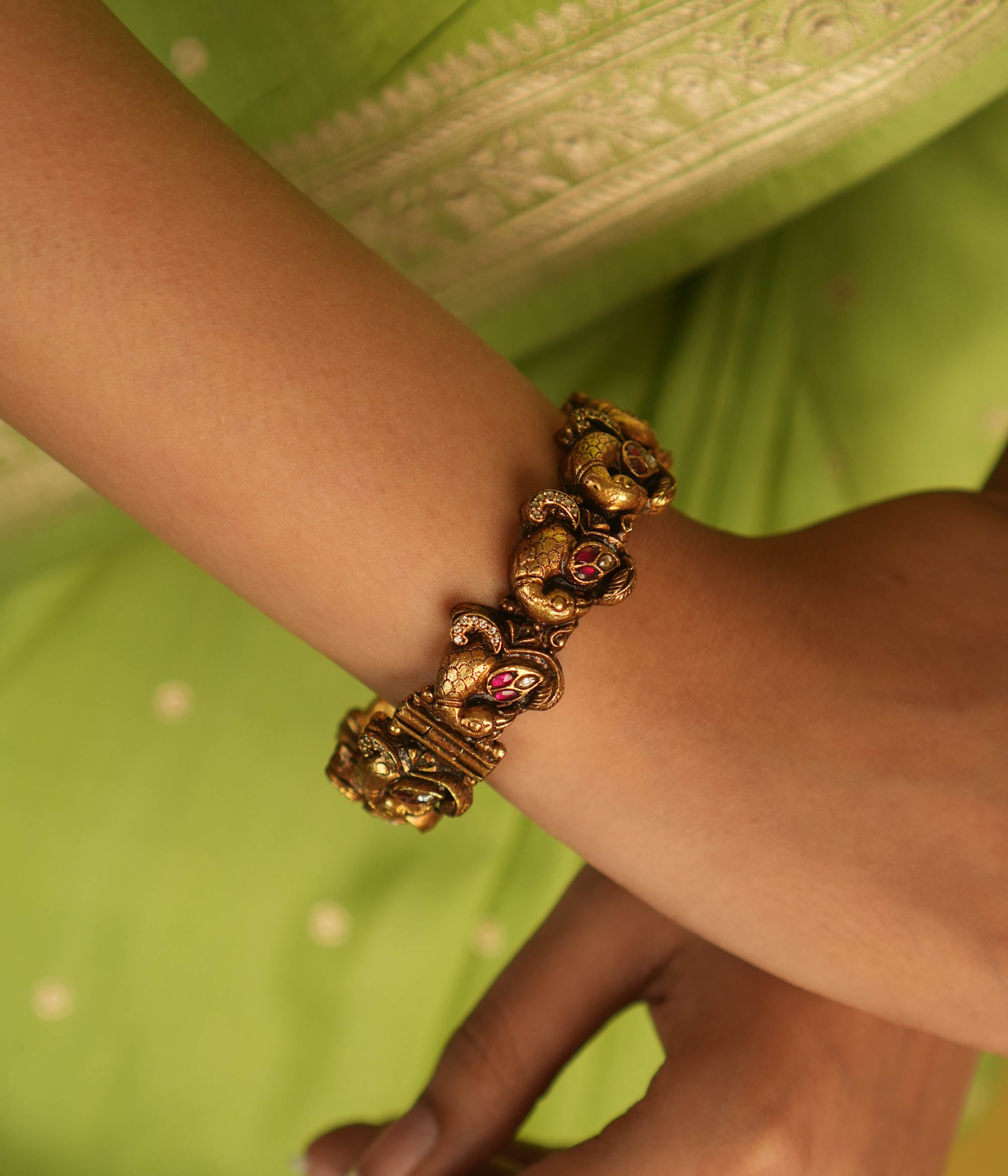Embrace royal elegance with this stunning antique gold bangle, adorned with vibrant red, white, and green Kundan stones, featuring an intricate peacock motif. The regal peacock comes to life in this piece, while the pink Kundan hues add a touch of grandeur. A perfect fusion of heritage and artistry, this bangle exudes timeless splendor.