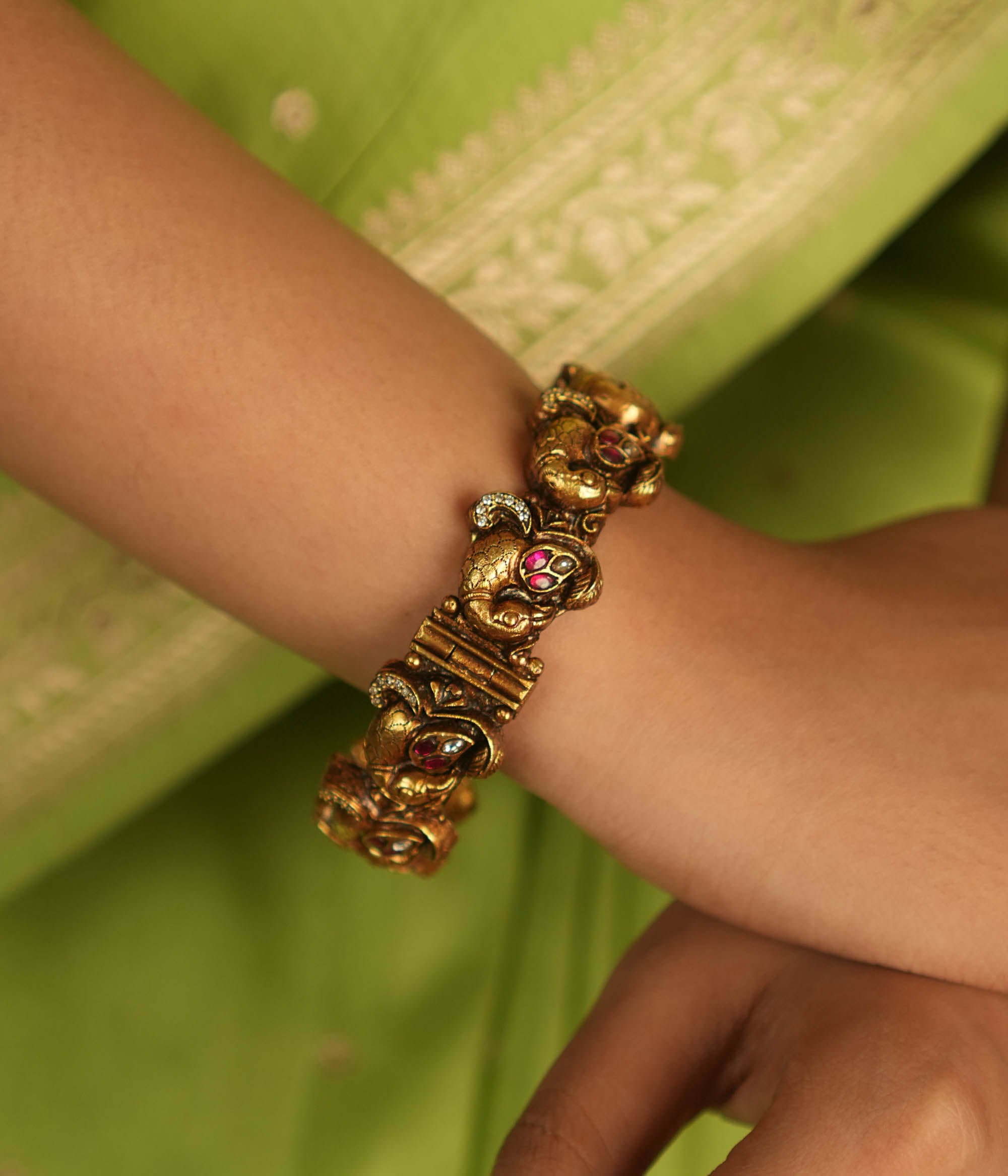 Embrace royal elegance with this stunning antique gold bangle, adorned with vibrant red, white, and green Kundan stones, featuring an intricate peacock motif. The regal peacock comes to life in this piece, while the pink Kundan hues add a touch of grandeur. A perfect fusion of heritage and artistry, this bangle exudes timeless splendor.