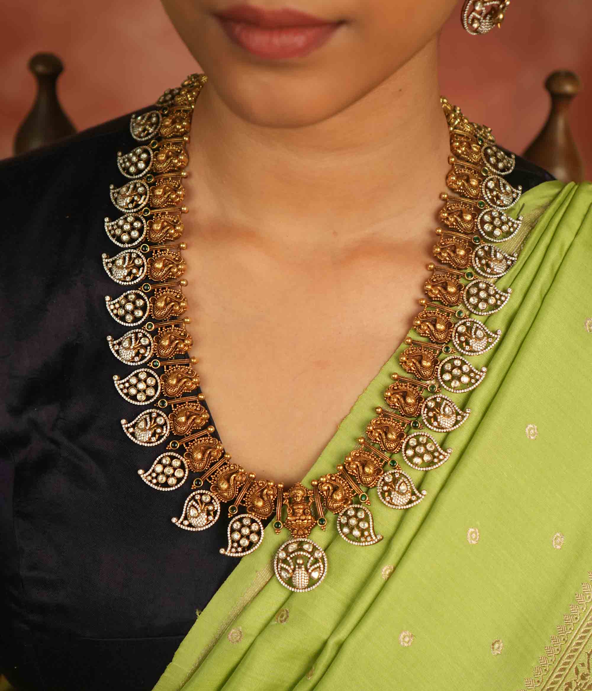 Temple whispers reborn! This gold-plated long necklace showcases regal peacock motifs and mango-shaped hangings adorned with polki, CZ, and green spinel stones. A timeless treasure that blends celestial grace with traditional charm.