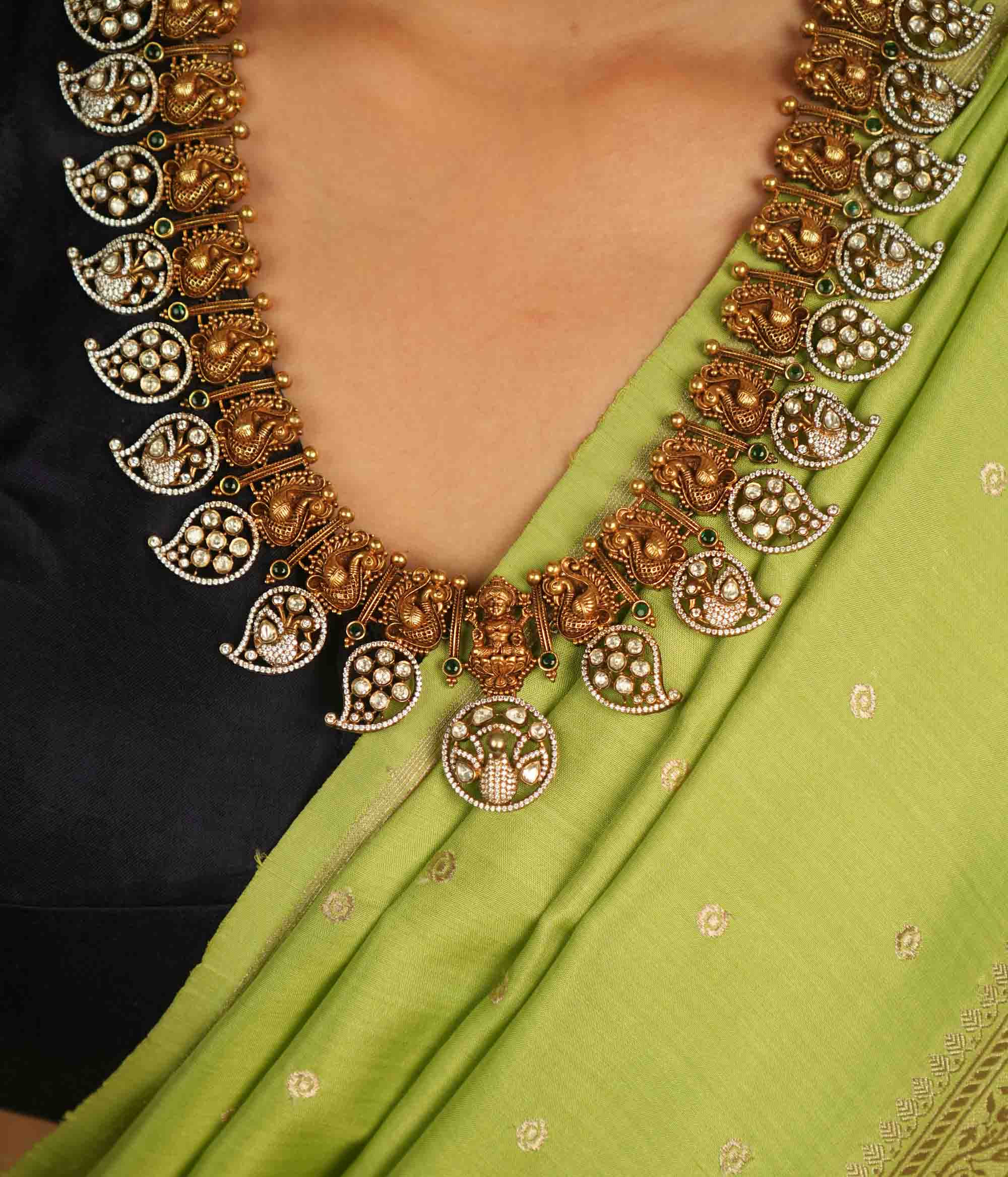 Temple whispers reborn! This gold-plated long necklace showcases regal peacock motifs and mango-shaped hangings adorned with polki, CZ, and green spinel stones. A timeless treasure that blends celestial grace with traditional charm.