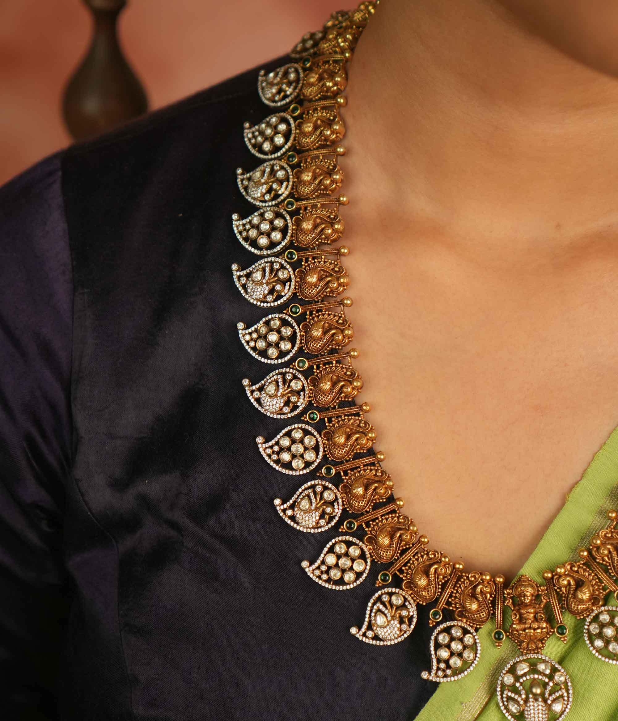 Temple whispers reborn! This gold-plated long necklace showcases regal peacock motifs and mango-shaped hangings adorned with polki, CZ, and green spinel stones. A timeless treasure that blends celestial grace with traditional charm.
