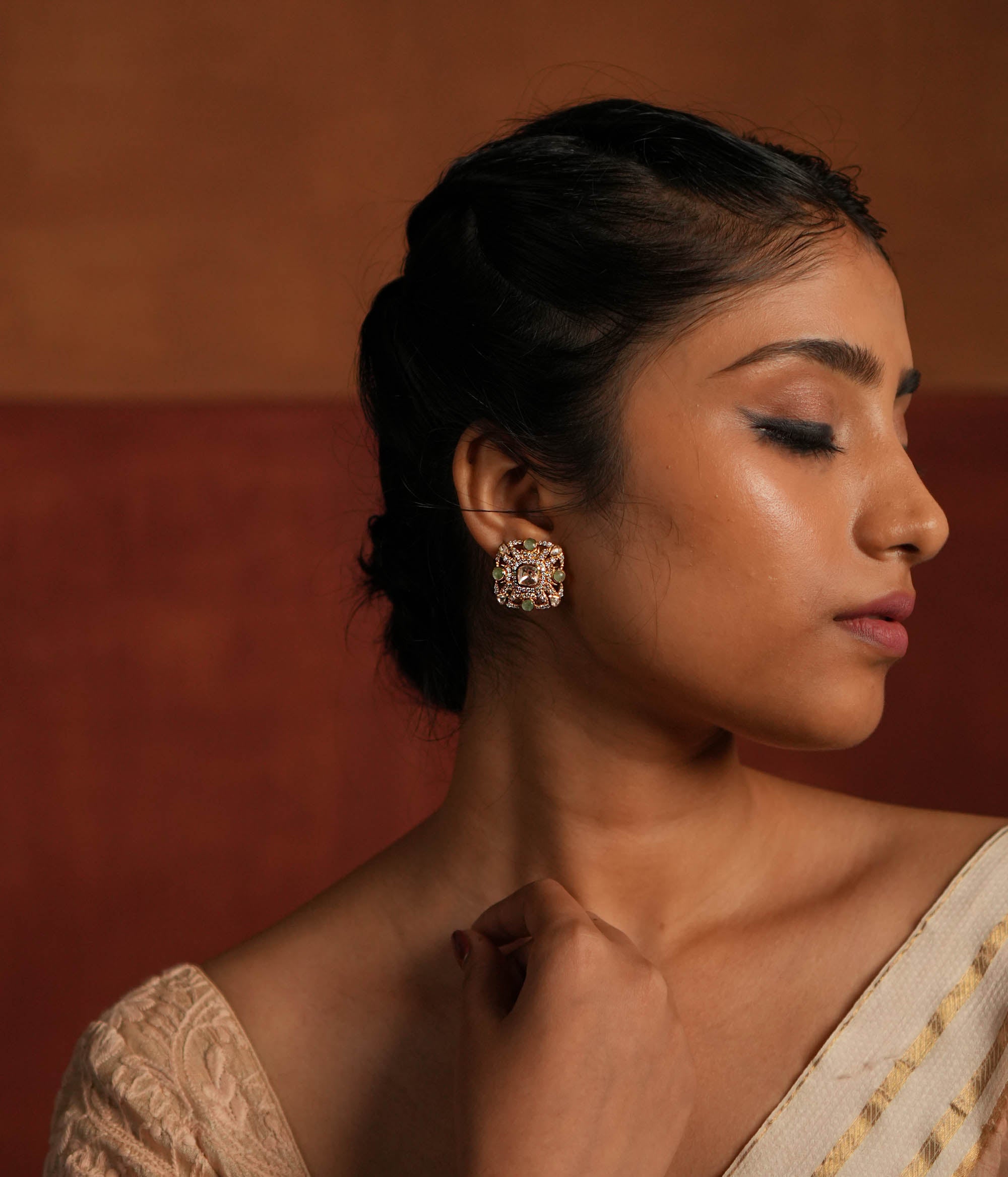 Elegant gold-plated silver stud earrings featuring a stunning square-shaped design. The center showcases a radiant Polki stone, beautifully encircled by layers of shimmering CZ stones. Adding to its charm, vibrant green gemstones are delicately placed within the CZ layers, enhancing the overall brilliance. A perfect blend of tradition and sophistication, ideal for any occasion.