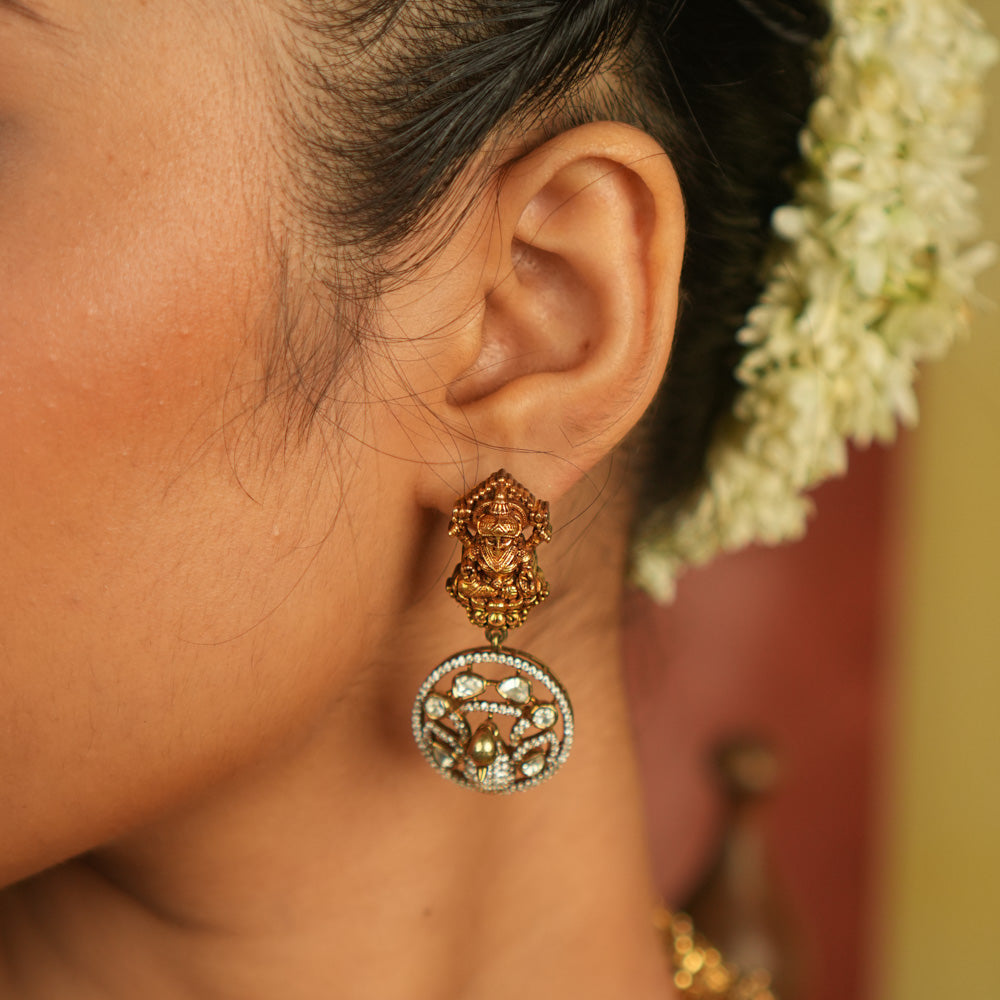 Divine elegance reborn! These gold-plated temple drop earrings feature a serene goddess Lakshmi motif on the stud, with a floral CZ stone frame below. A celestial tribute to timeless artistry and cultural grace.