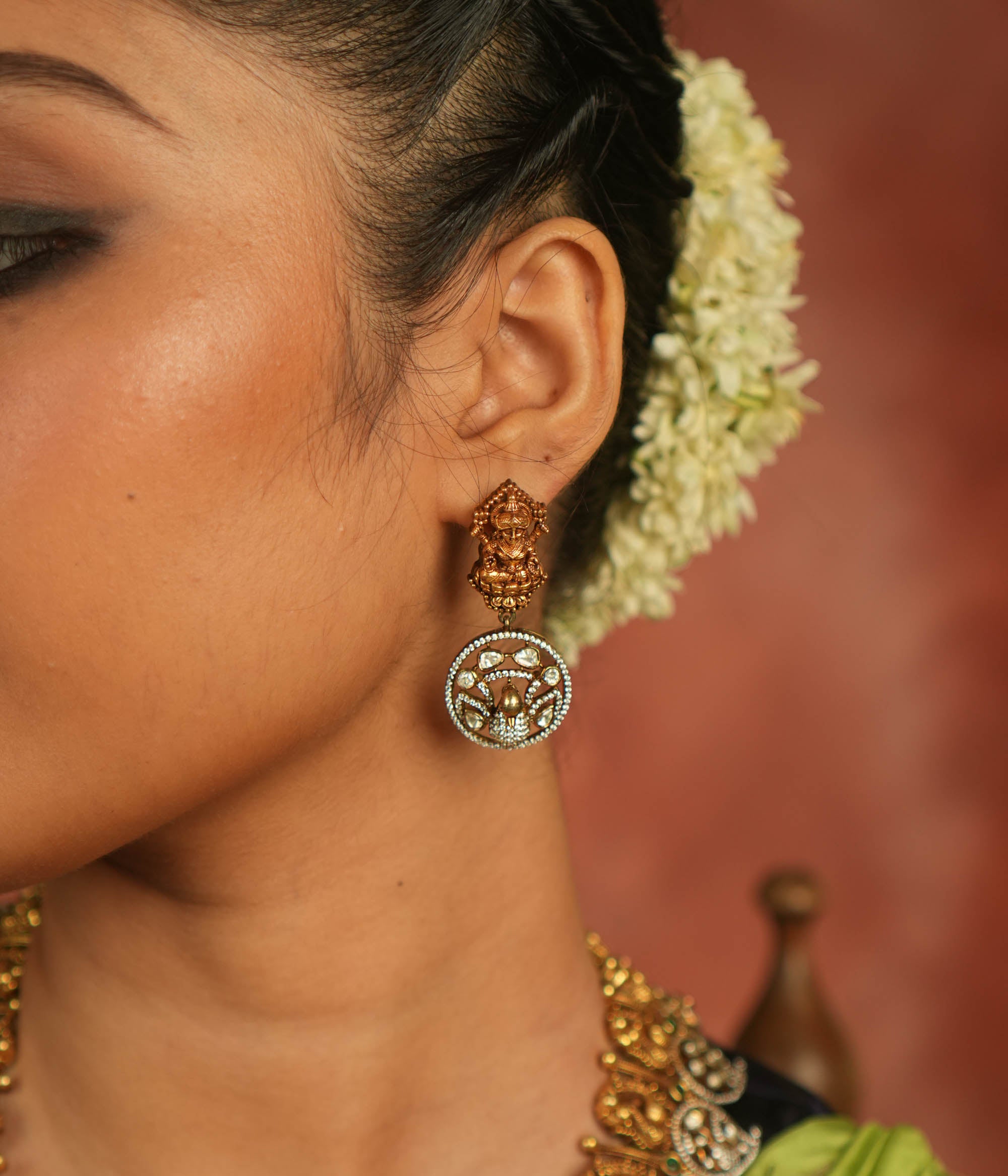 Divine elegance reborn! These gold-plated temple drop earrings feature a serene goddess Lakshmi motif on the stud, with a floral CZ stone frame below. A celestial tribute to timeless artistry and cultural grace.