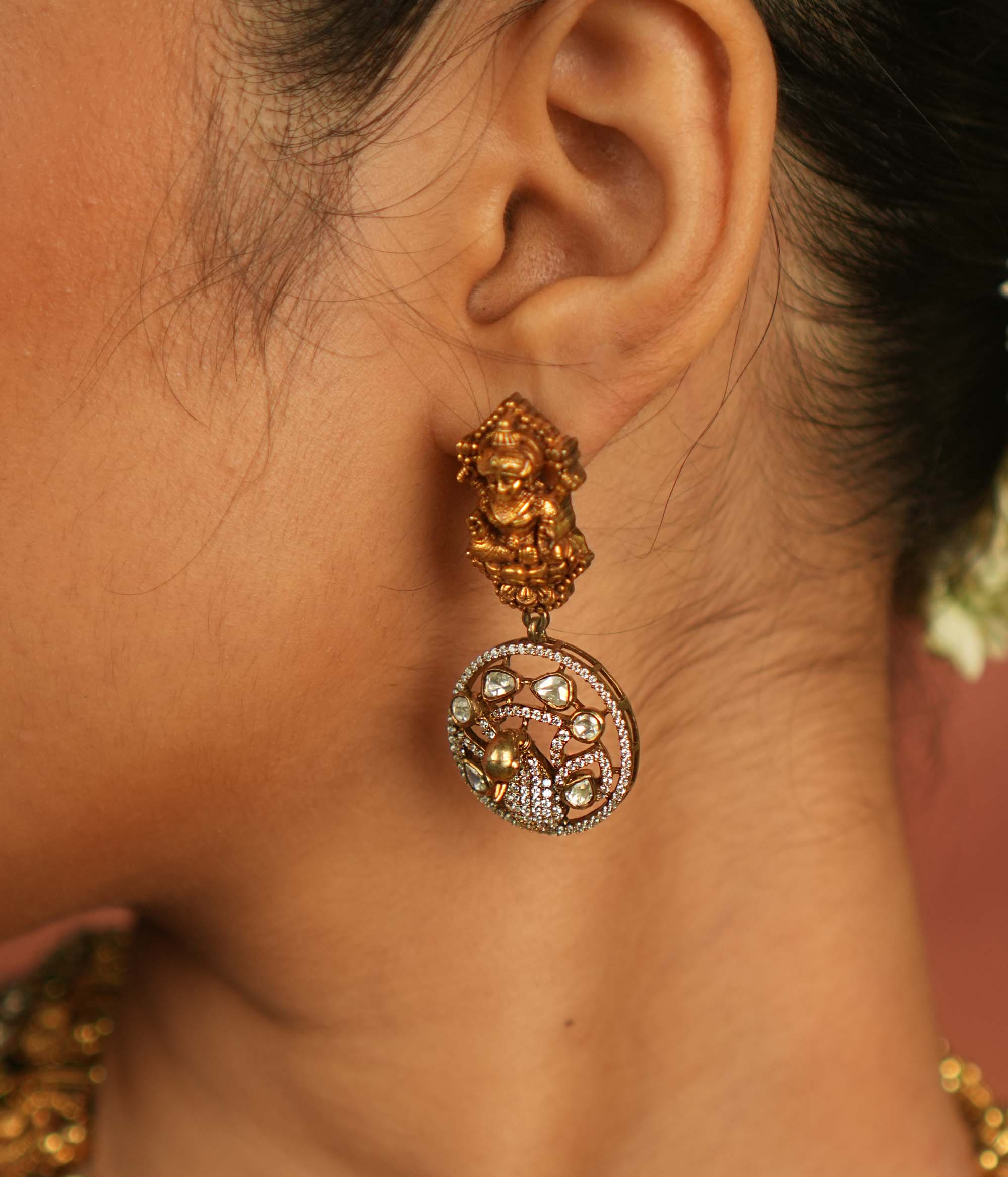 Divine elegance reborn! These gold-plated temple drop earrings feature a serene goddess Lakshmi motif on the stud, with a floral CZ stone frame below. A celestial tribute to timeless artistry and cultural grace.