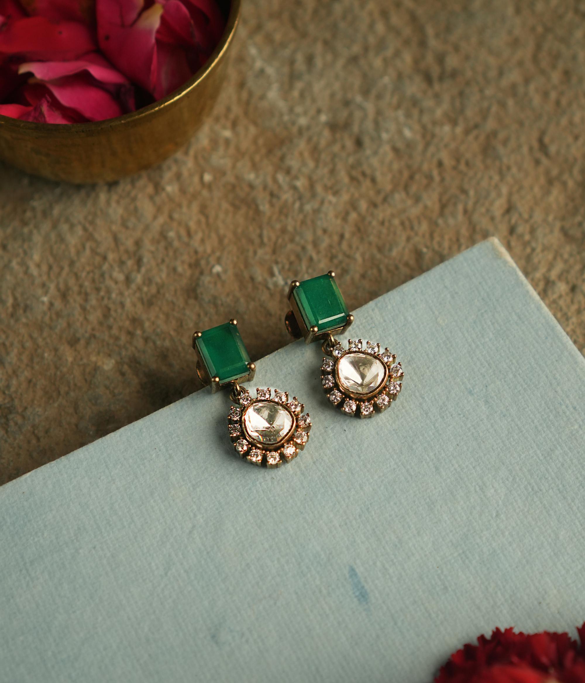 Amidst the vibrant charm of a bustling bazaar, this minimal floral stud with a radiant green cut stone at its heart, encircled by shimmering polki stones, whispers timeless elegance.