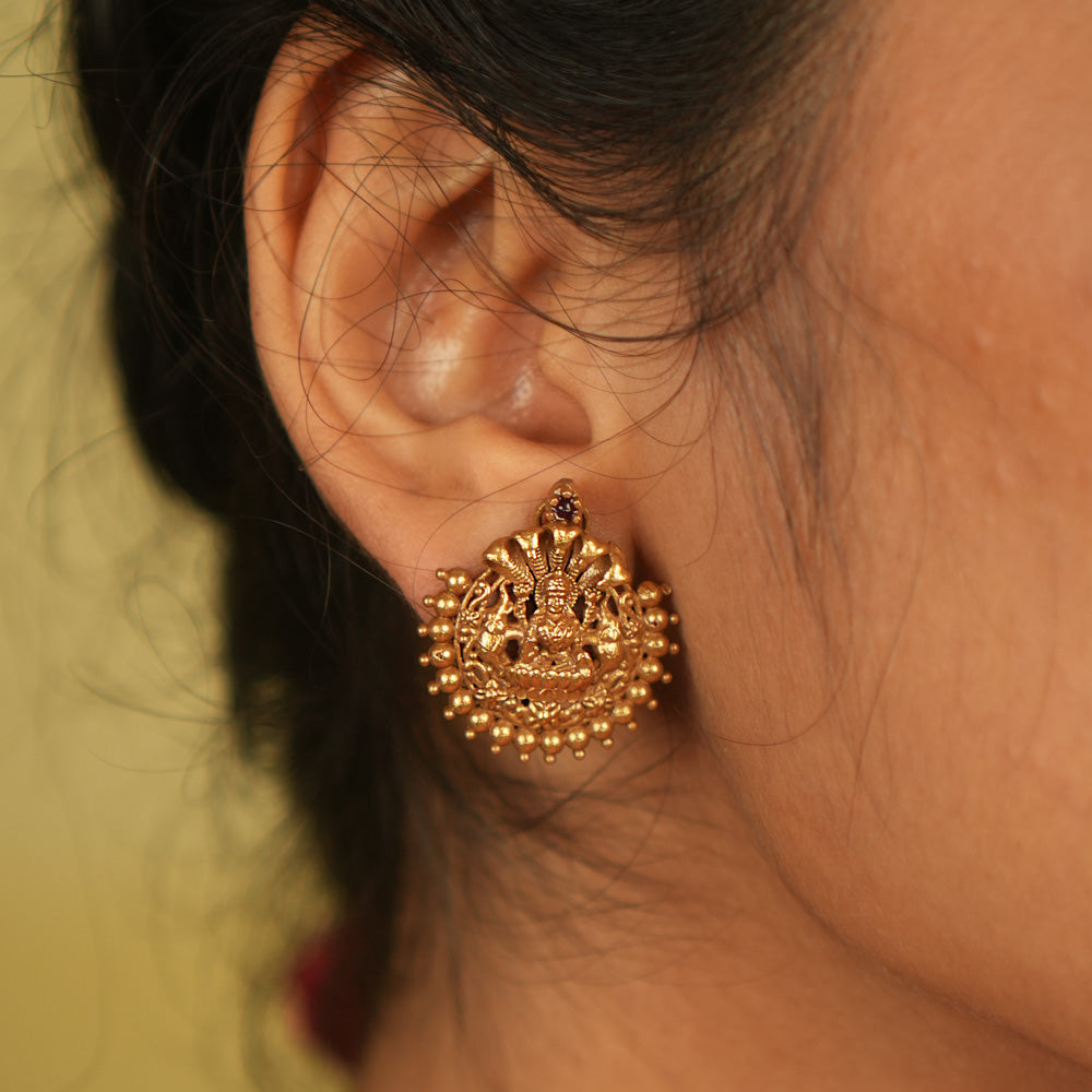 Divine elegance redefined! These gold-plated stud earrings feature Goddess Lakshmi, adorned with delicate golden beads. A perfect blend of tradition and modern charm.