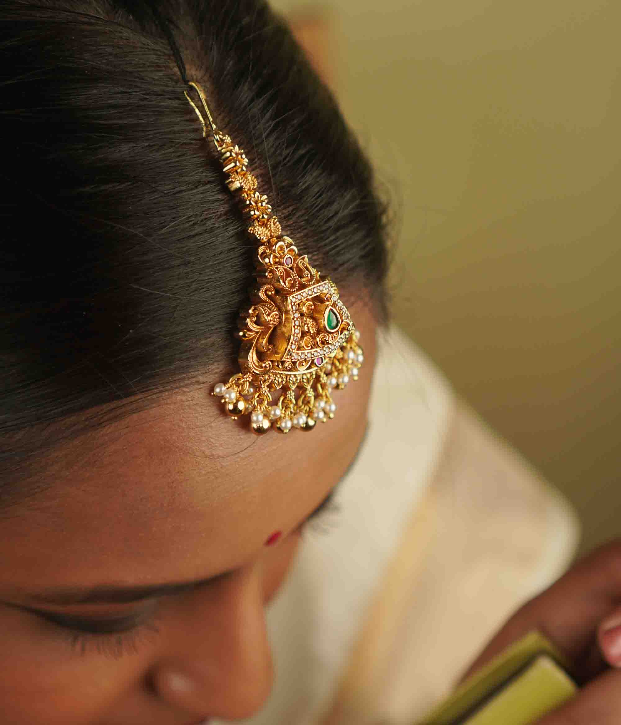 Yarima Maangtika: An embodiment of elegance. Crafted in gold-plated silver, this tikka features red and green spinel stones, CZ stones, and pearls, designed in a vintage Chettinad style. A cherished keepsake to affirm your timeless beauty.