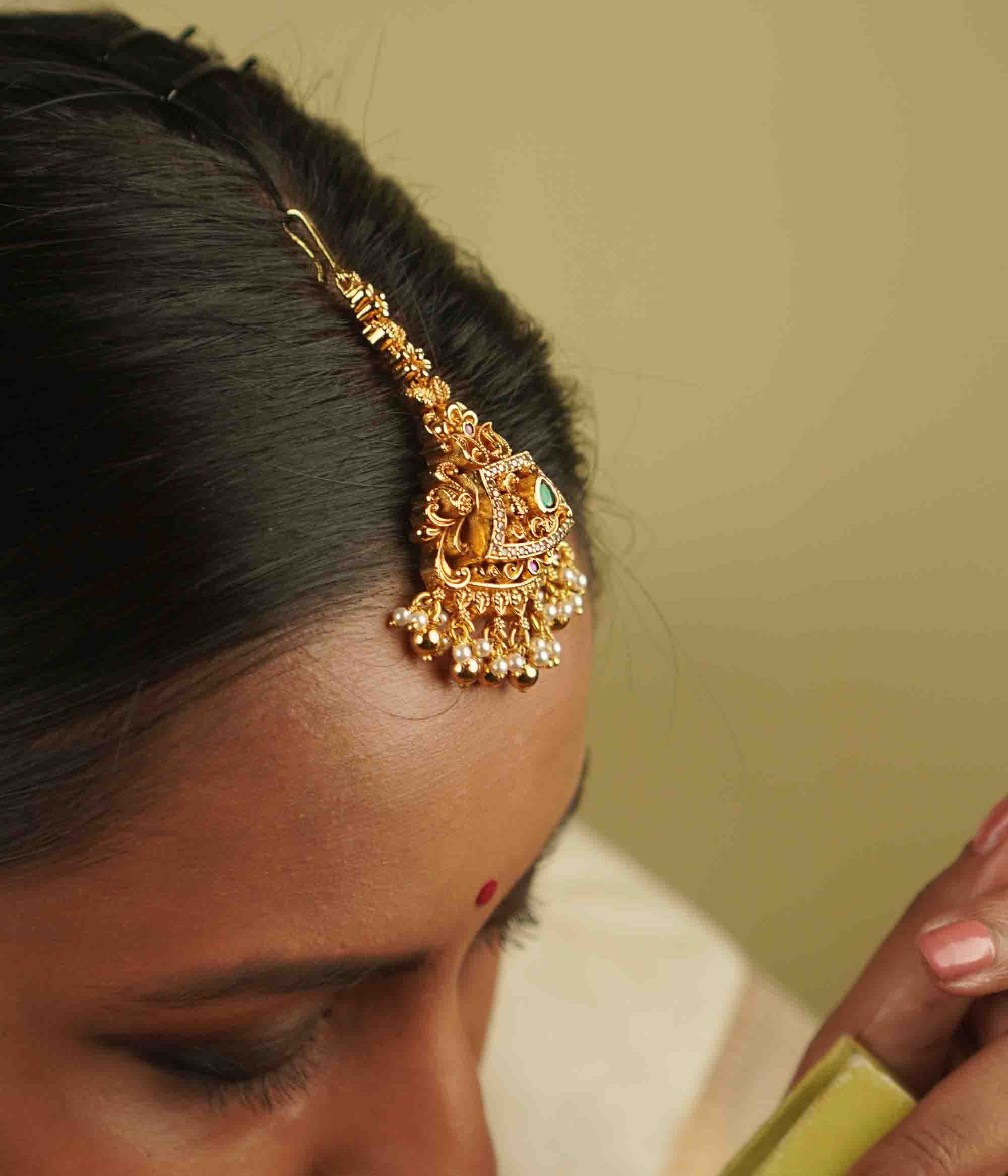 Yarima Maangtika: An embodiment of elegance. Crafted in gold-plated silver, this tikka features red and green spinel stones, CZ stones, and pearls, designed in a vintage Chettinad style. A cherished keepsake to affirm your timeless beauty.