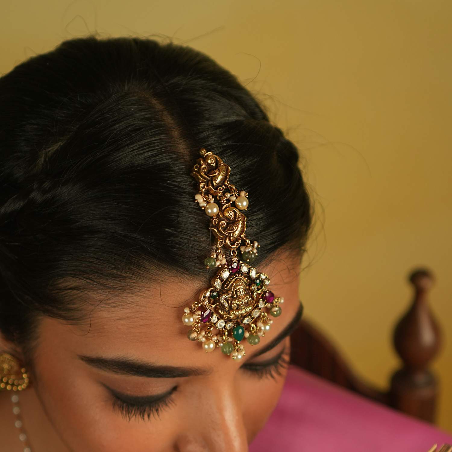 This traditional Lakshmi Tikka, featuring intricate peacock and goddess motifs, is adorned with vibrant red and green spinel stones. Accented by lustrous pearls, it exudes timeless elegance and spiritual grace, making it a perfect blend of heritage and beauty.