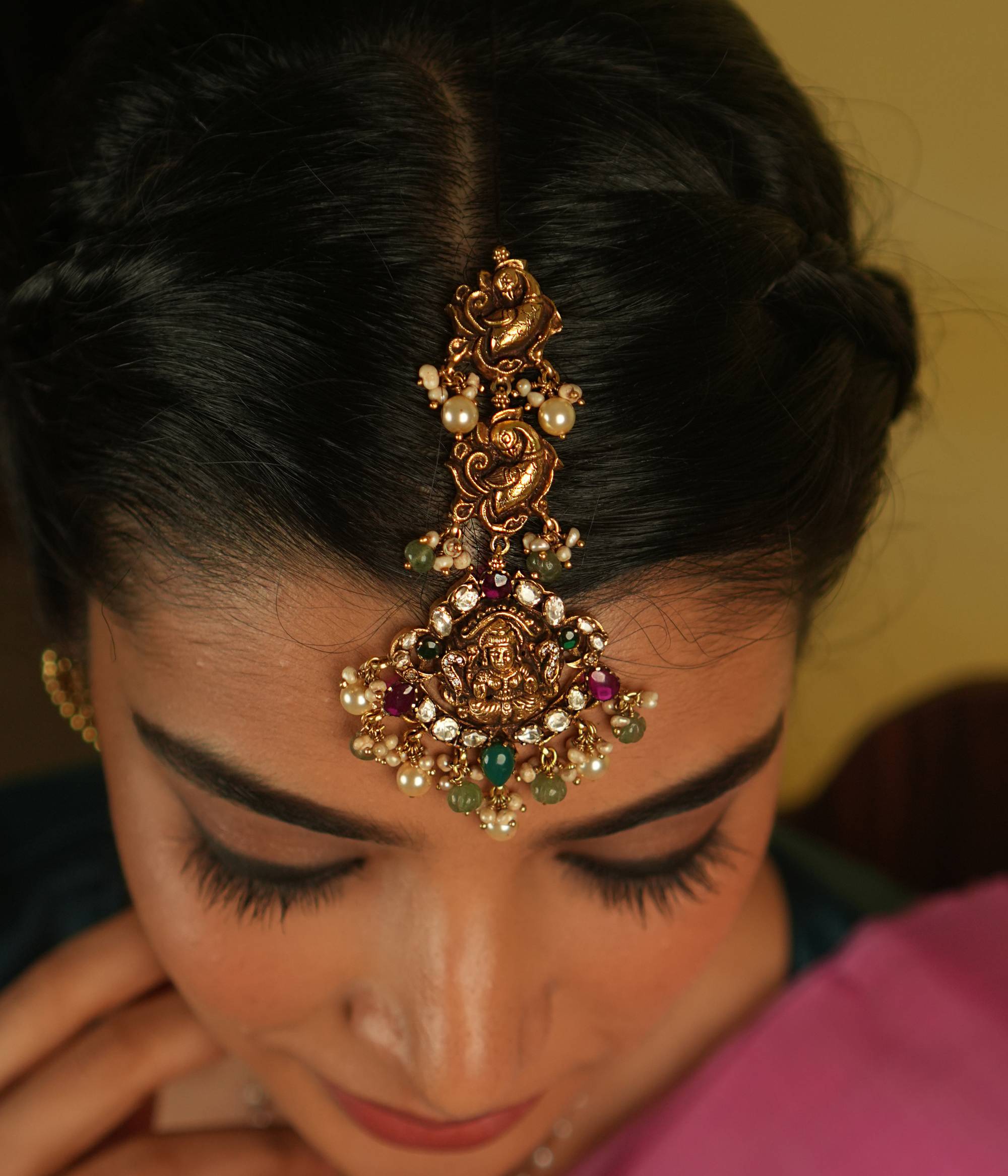 This traditional Lakshmi Tikka, featuring intricate peacock and goddess motifs, is adorned with vibrant red and green spinel stones. Accented by lustrous pearls, it exudes timeless elegance and spiritual grace, making it a perfect blend of heritage and beauty.