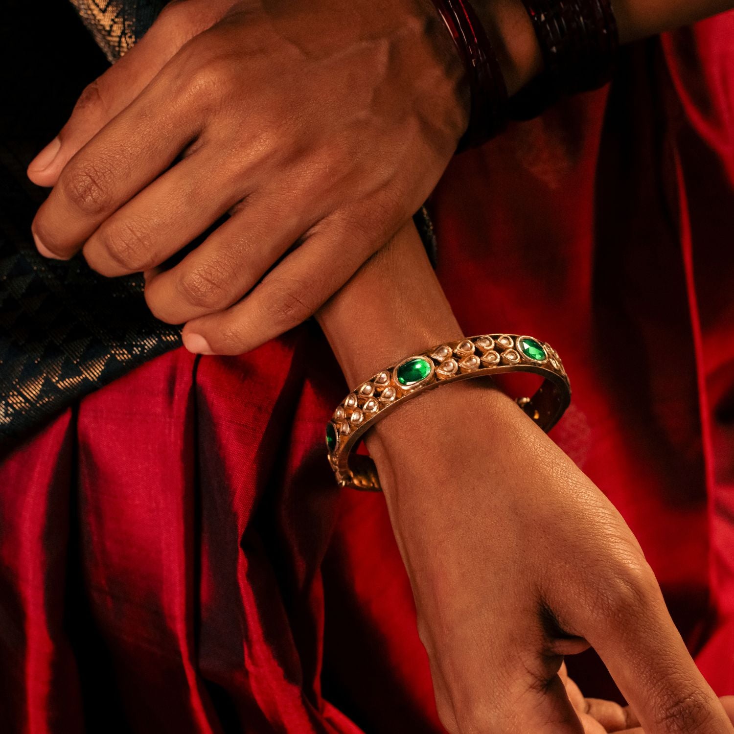 Gold-plated silver bangle adorned with elegantly arranged white sapphires and emeralds in delicate drop-shaped designs. The intricate setting of gemstones enhances its sophisticated appeal, making it a perfect blend of tradition and elegance.