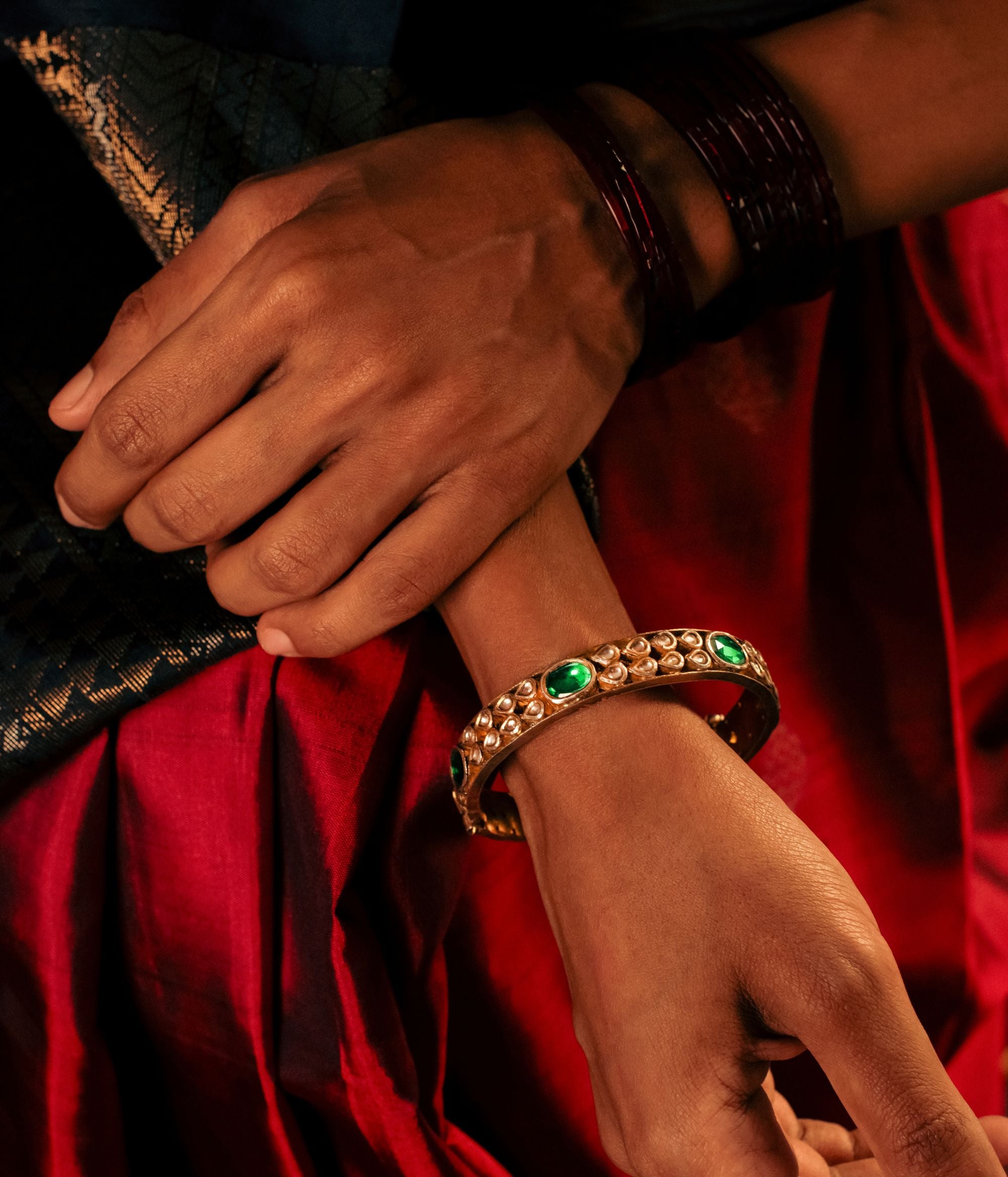 Gold-plated silver bangle adorned with elegantly arranged white sapphires and emeralds in delicate drop-shaped designs. The intricate setting of gemstones enhances its sophisticated appeal, making it a perfect blend of tradition and elegance.