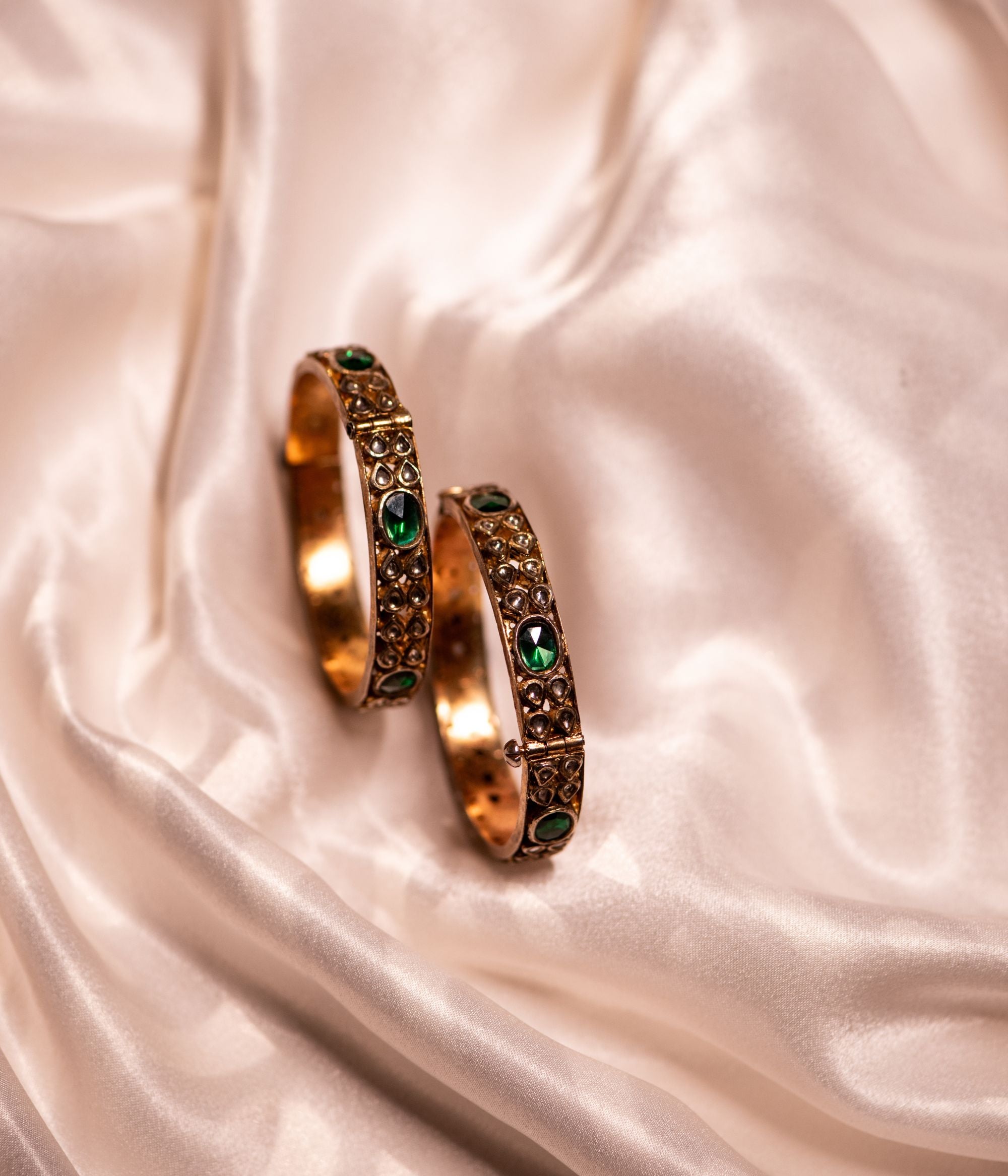 Gold-plated silver bangle adorned with elegantly arranged white sapphires and emeralds in delicate drop-shaped designs. The intricate setting of gemstones enhances its sophisticated appeal, making it a perfect blend of tradition and elegance.
