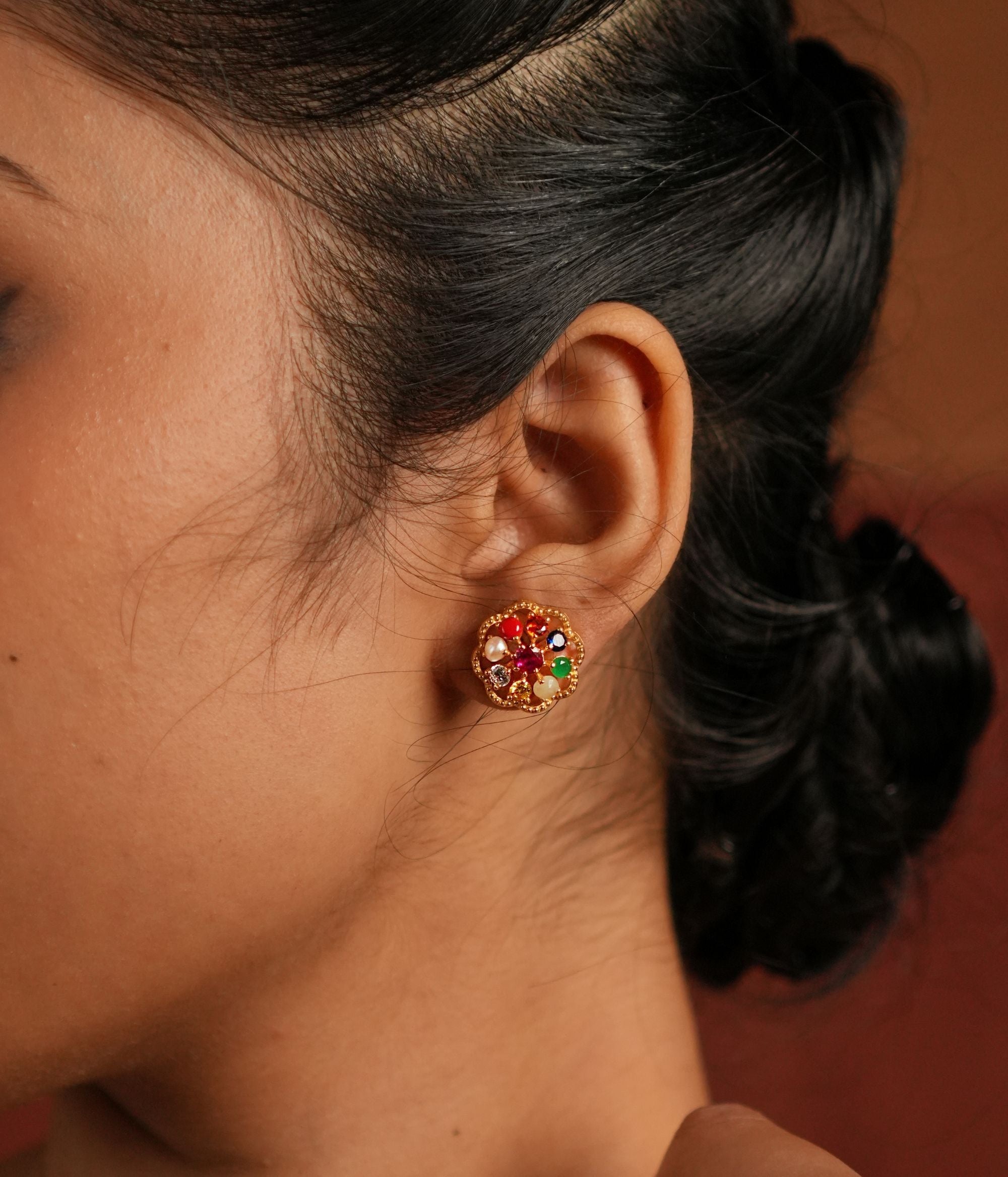 A beautifully crafted gold-plated silver stud earring in a delicate round shape, featuring vibrant Navratna stones arranged in a floral design. The center is adorned with a dazzling CZ stone, enhancing its elegance. This timeless piece blends tradition with sophistication, making it a perfect accessory for any occasion.