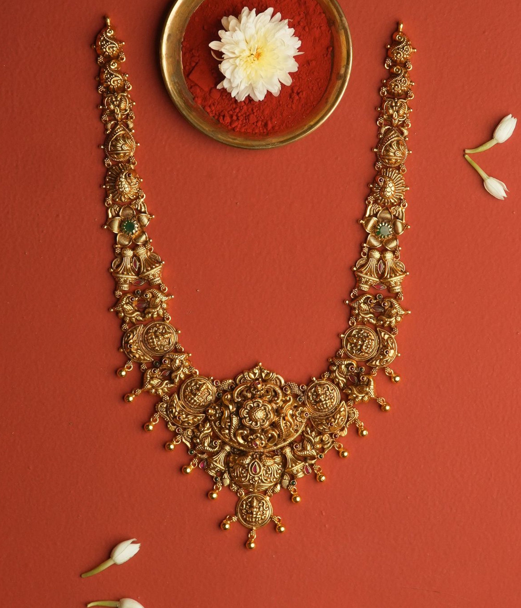 Ornate gold necklace on a red background with a white flower.