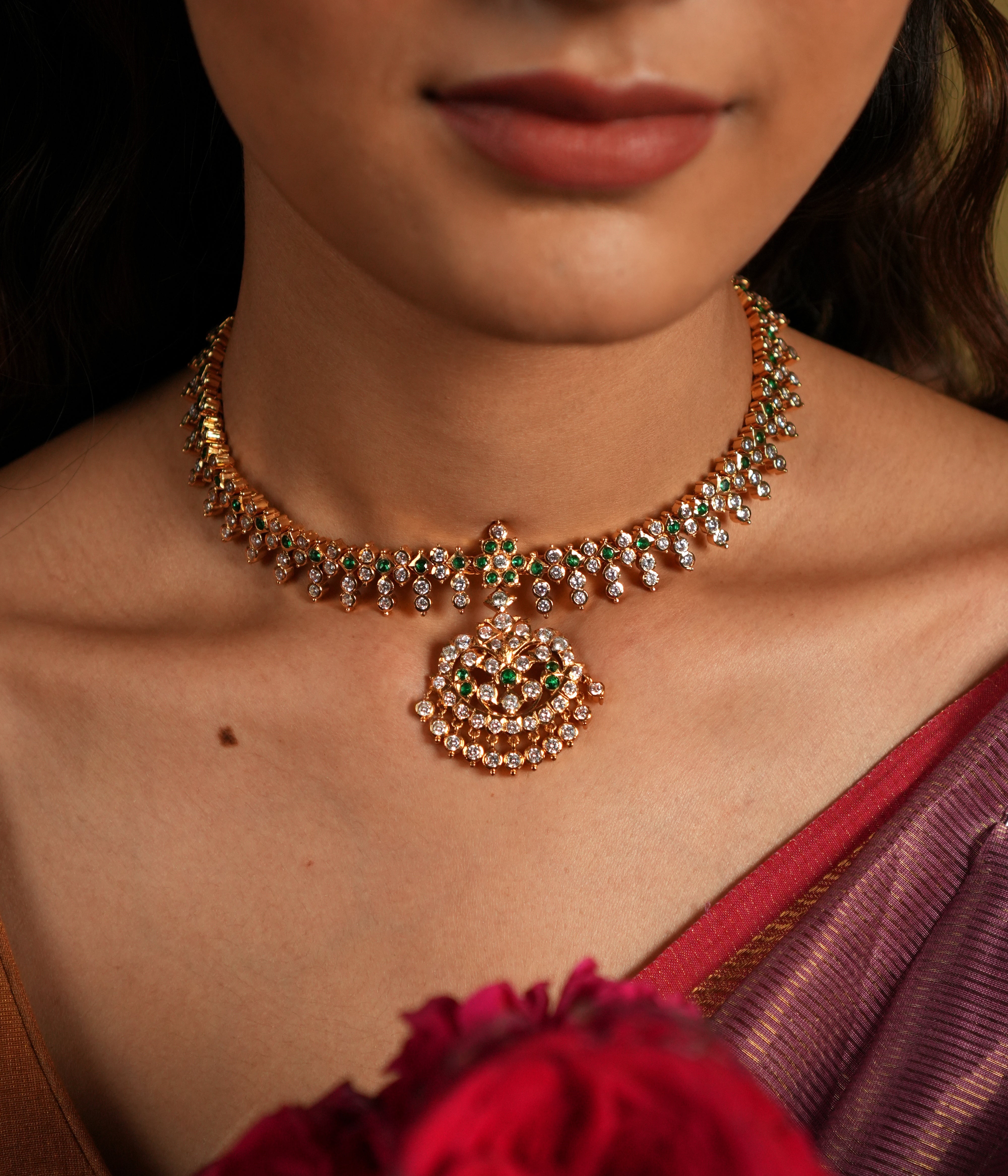 This exquisite Swarovski choker, crafted from 92.5 sterling silver with a rich 22-carat gold plating, is adorned with traditional floral motifs that whisper vintage Chettinad elegance. The intricate detailing and shimmering Swarovski stones bring a timeless charm, perfectly blending heritage craftsmanship with modern sophistication. Ideal for weddings and festive occasions, this choker gracefully accentuates your neckline, adding a touch of regal allure to any ensemble.