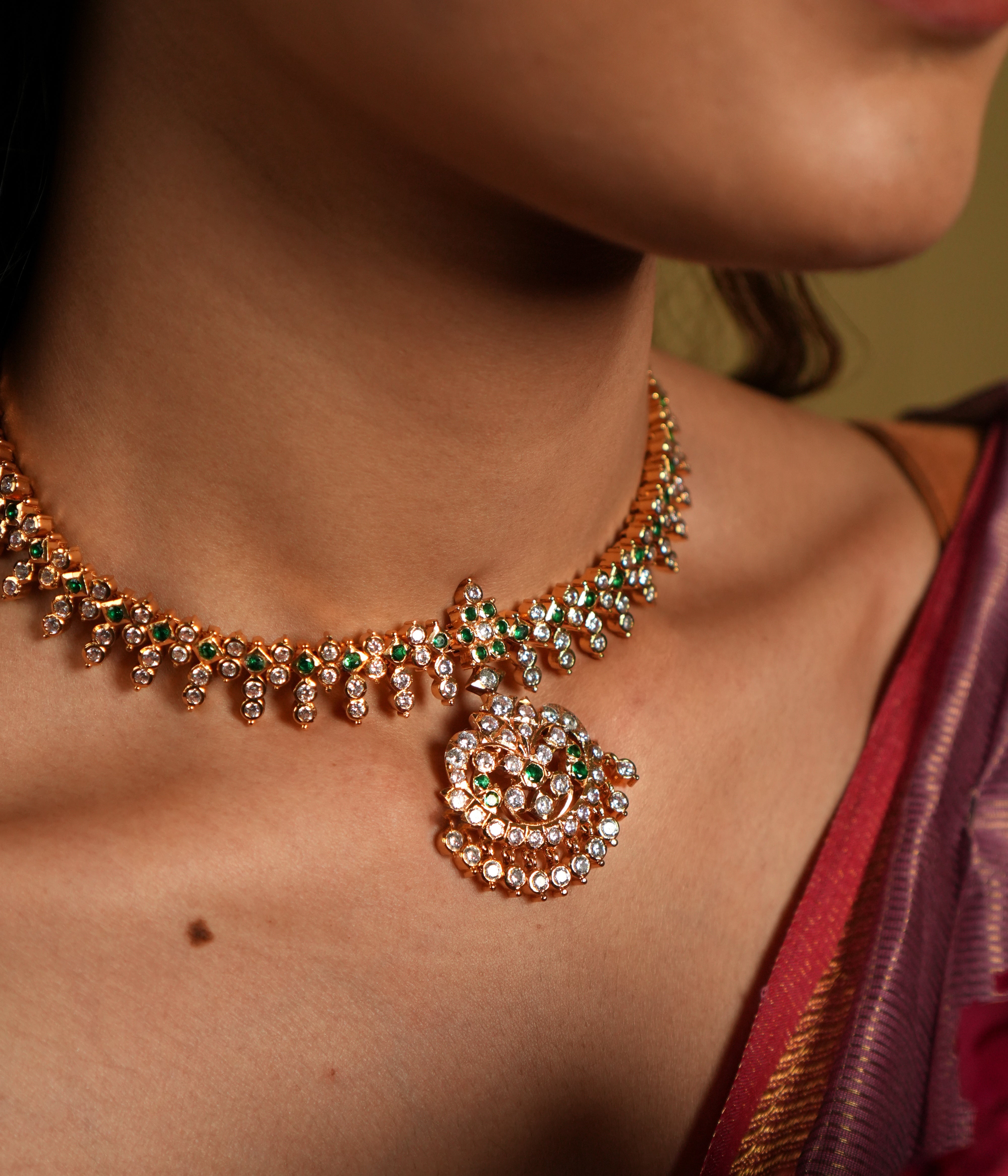 This exquisite Swarovski choker, crafted from 92.5 sterling silver with a rich 22-carat gold plating, is adorned with traditional floral motifs that whisper vintage Chettinad elegance. The intricate detailing and shimmering Swarovski stones bring a timeless charm, perfectly blending heritage craftsmanship with modern sophistication. Ideal for weddings and festive occasions, this choker gracefully accentuates your neckline, adding a touch of regal allure to any ensemble.