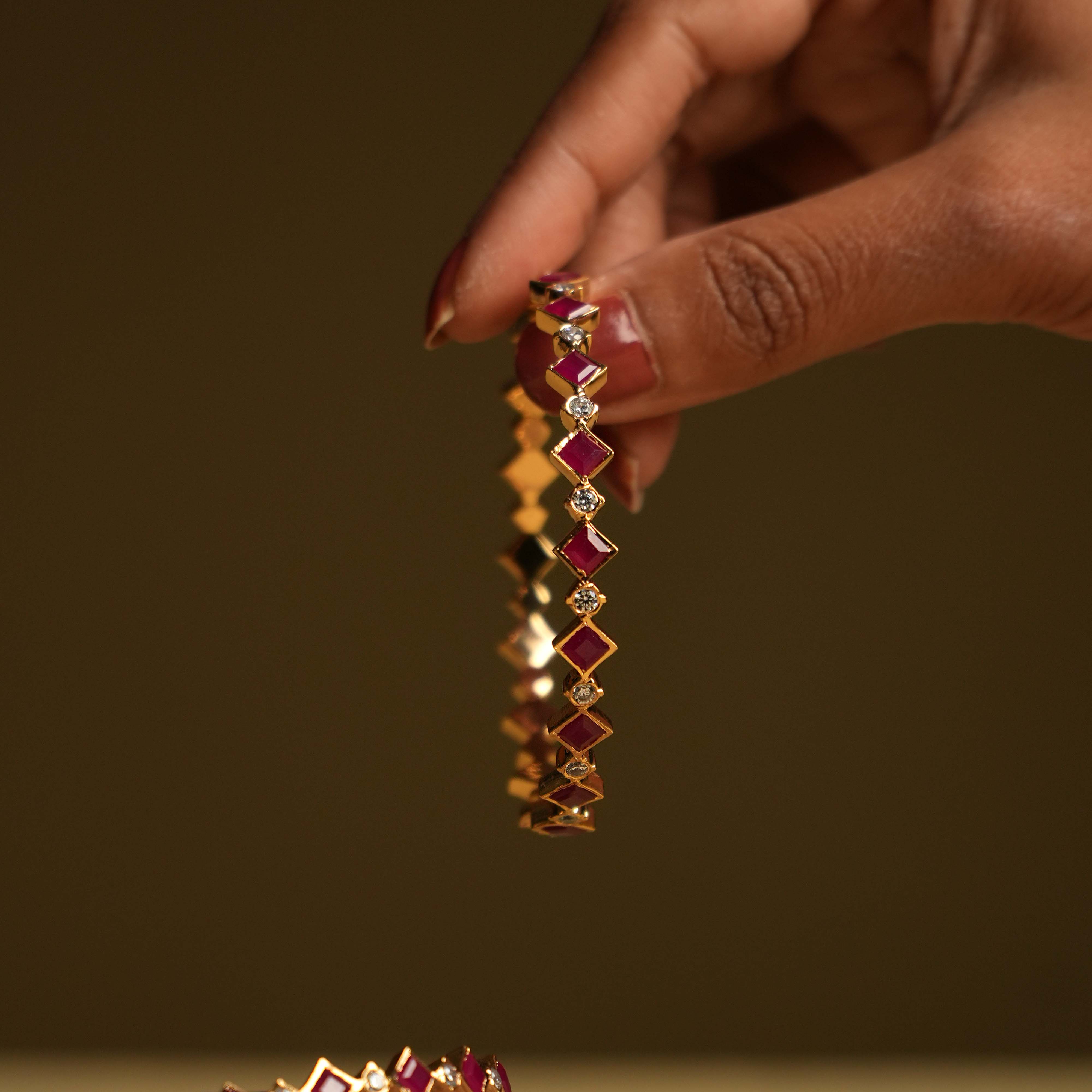 A pair of minimalist 92.5 sterling silver bangles with an insert type closure, featuring alternating square-cut red gemstones and round white stones, creating a mesmerizing dance of color and light and embodying subtle luxury with a touch of playful, modern flair.