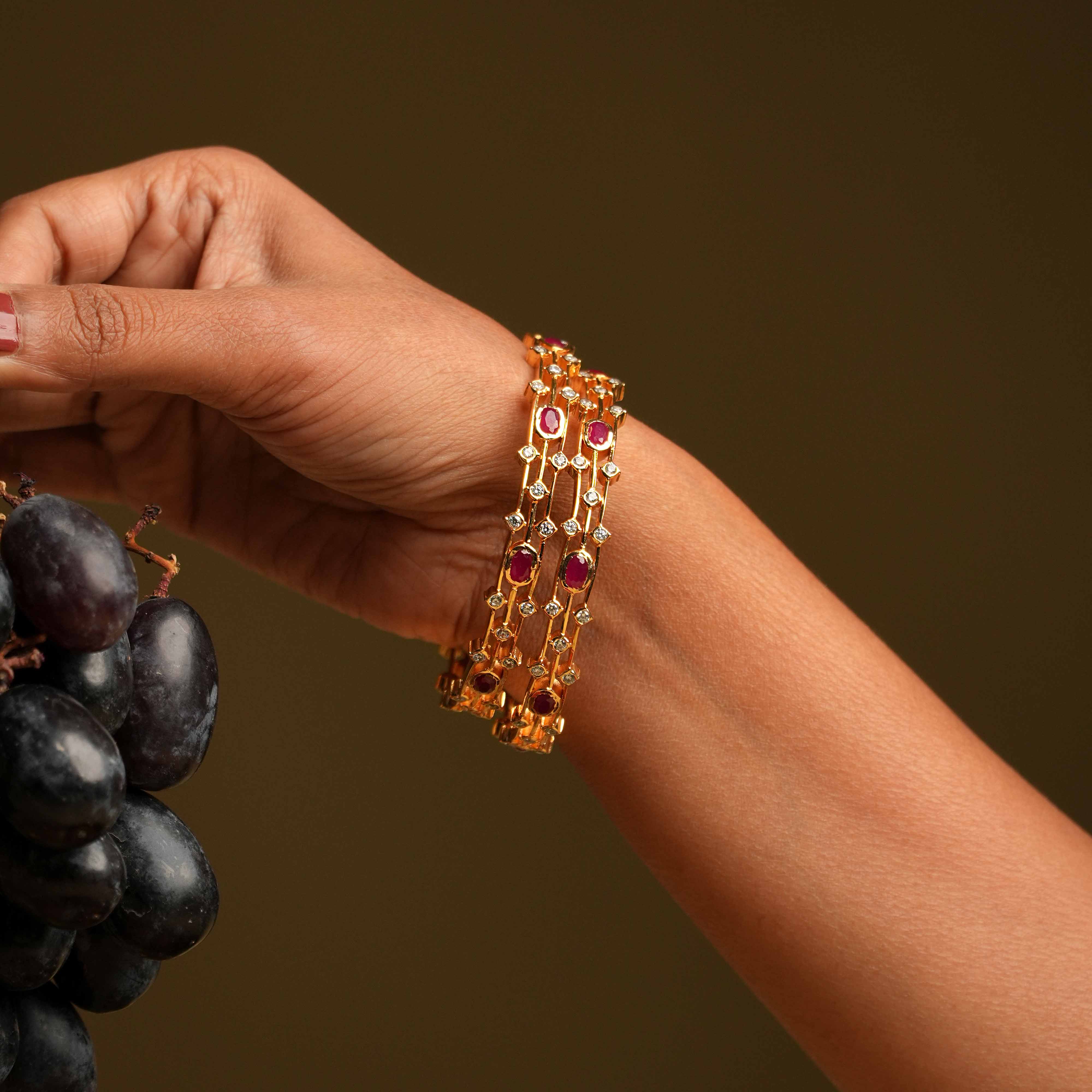 A triple-lined 92.5 sterling silver bangle with an insert type closure, showcasing clusters of moissanite and red oval gemstones intricately set with traditional diamond setting techniques, blending majestic elegance with modern sophistication.