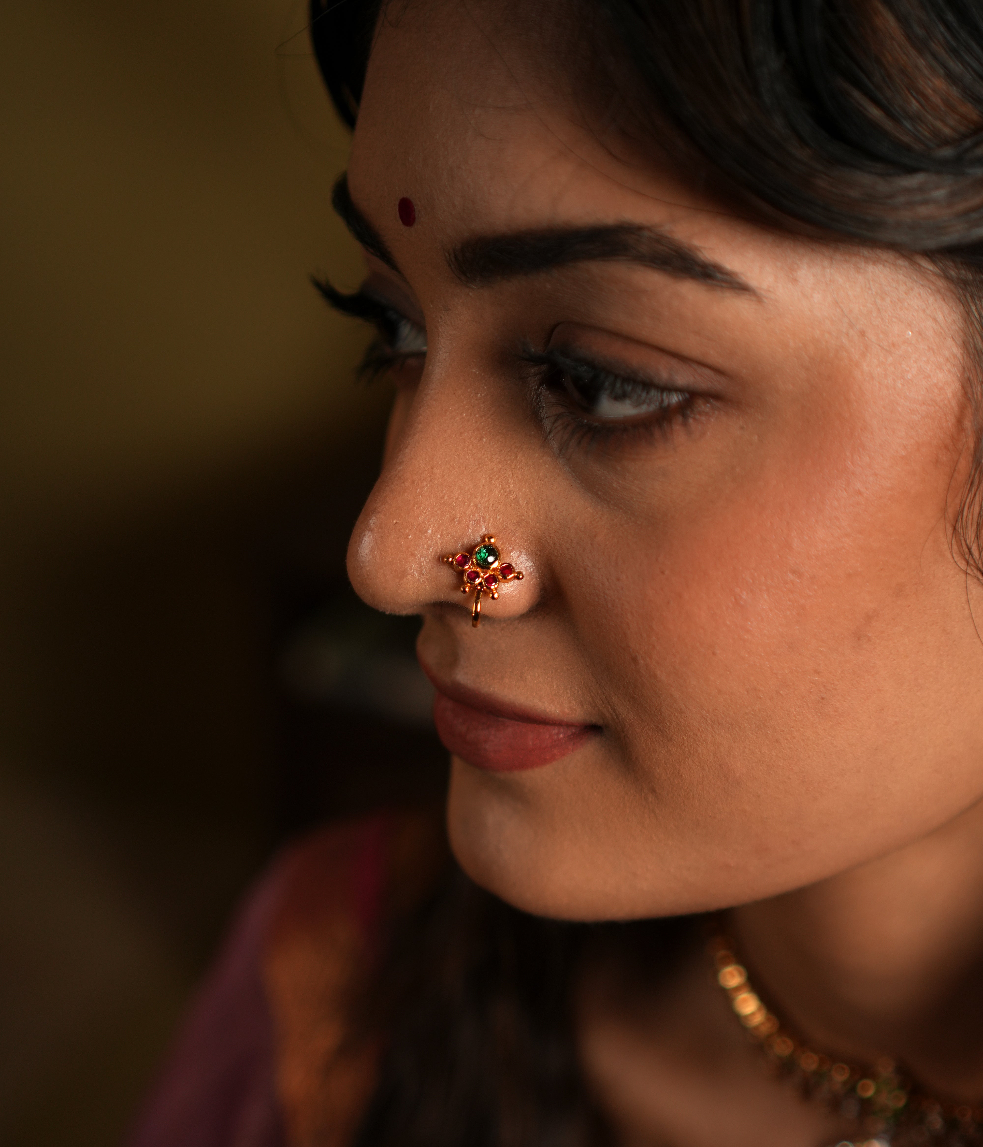 This image features a beautifully crafted 92.5 sterling silver nose pin with an elegant gold-plated finish. The nose pin is designed in a delicate floral pattern, with a striking green stone at its center, adding a subtle yet captivating charm.