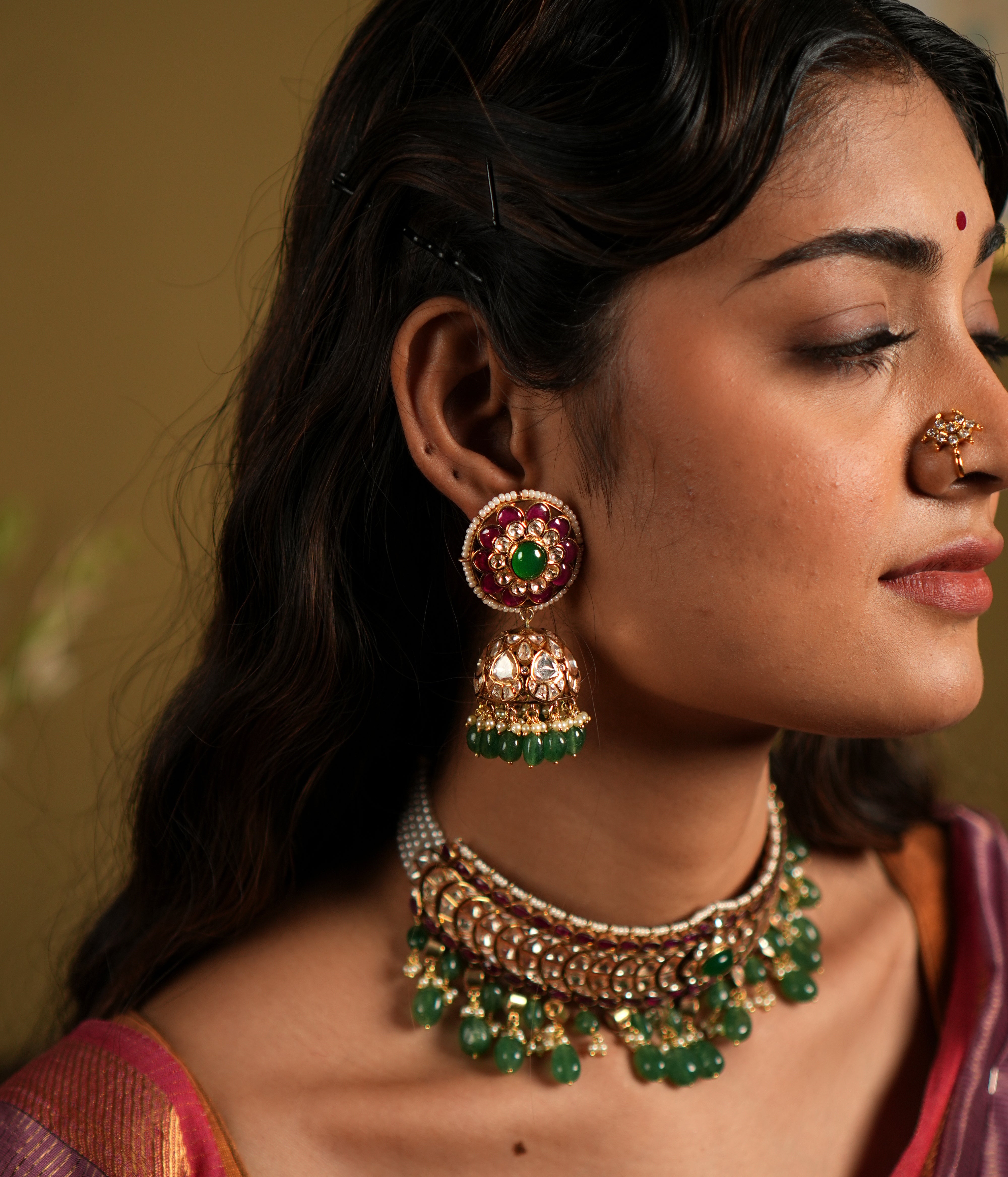 This image showcases an exquisite pair of Moissanite Polki Jhumkas crafted from 92.5 sterling silver and finished with a luxurious gold plating. The earrings feature a vibrant combination of deep red and green stones, with intricate Polki work that exudes traditional elegance.