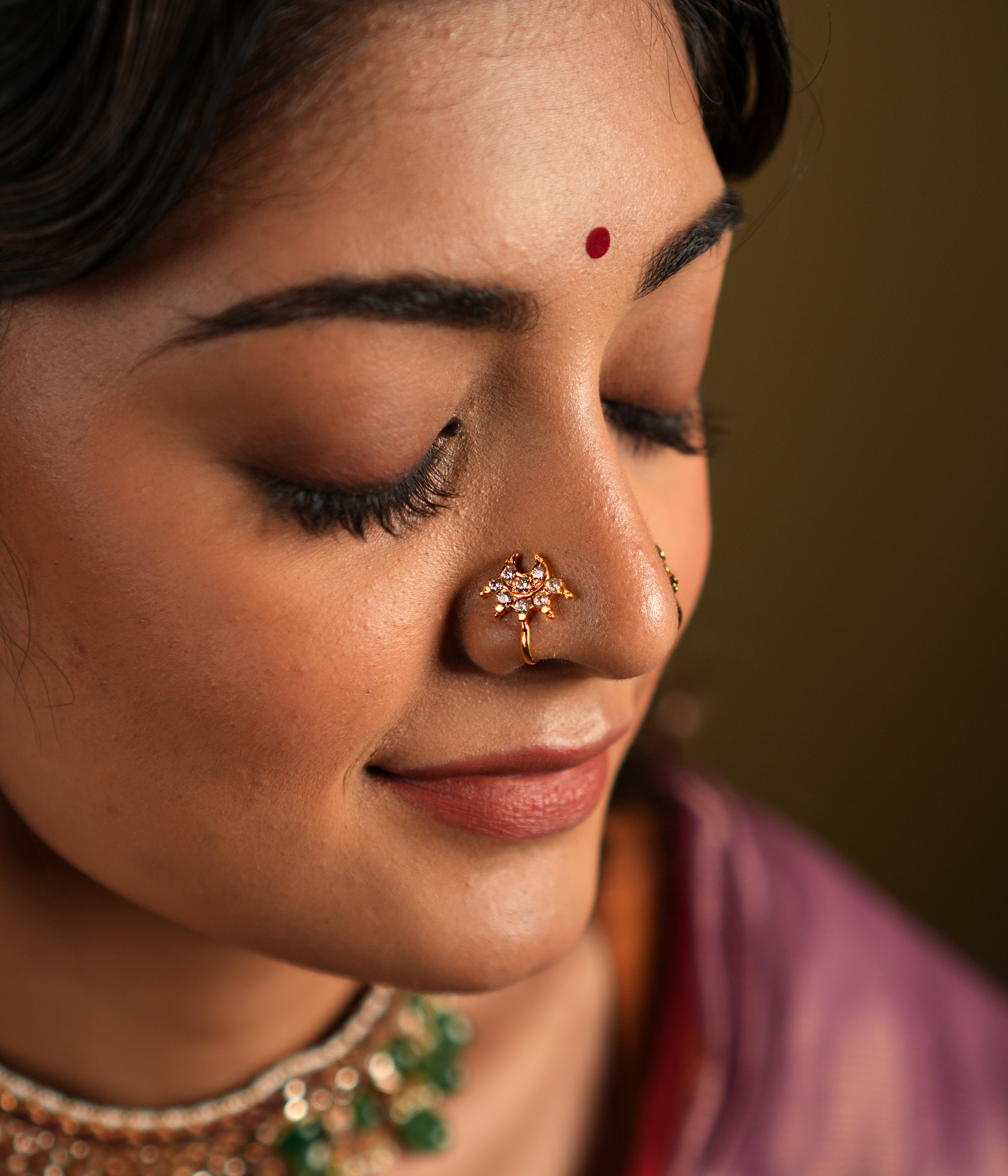 features a stunning 92.5 sterling silver nose pin with an elegant gold-plated finish. The nose pin is designed in a unique, intricate pattern adorned with sparkling stones, offering a delicate yet eye-catching appeal. Its refined craftsmanship and graceful design make it a versatile accessory, perfect for traditional attire or festive occasions.