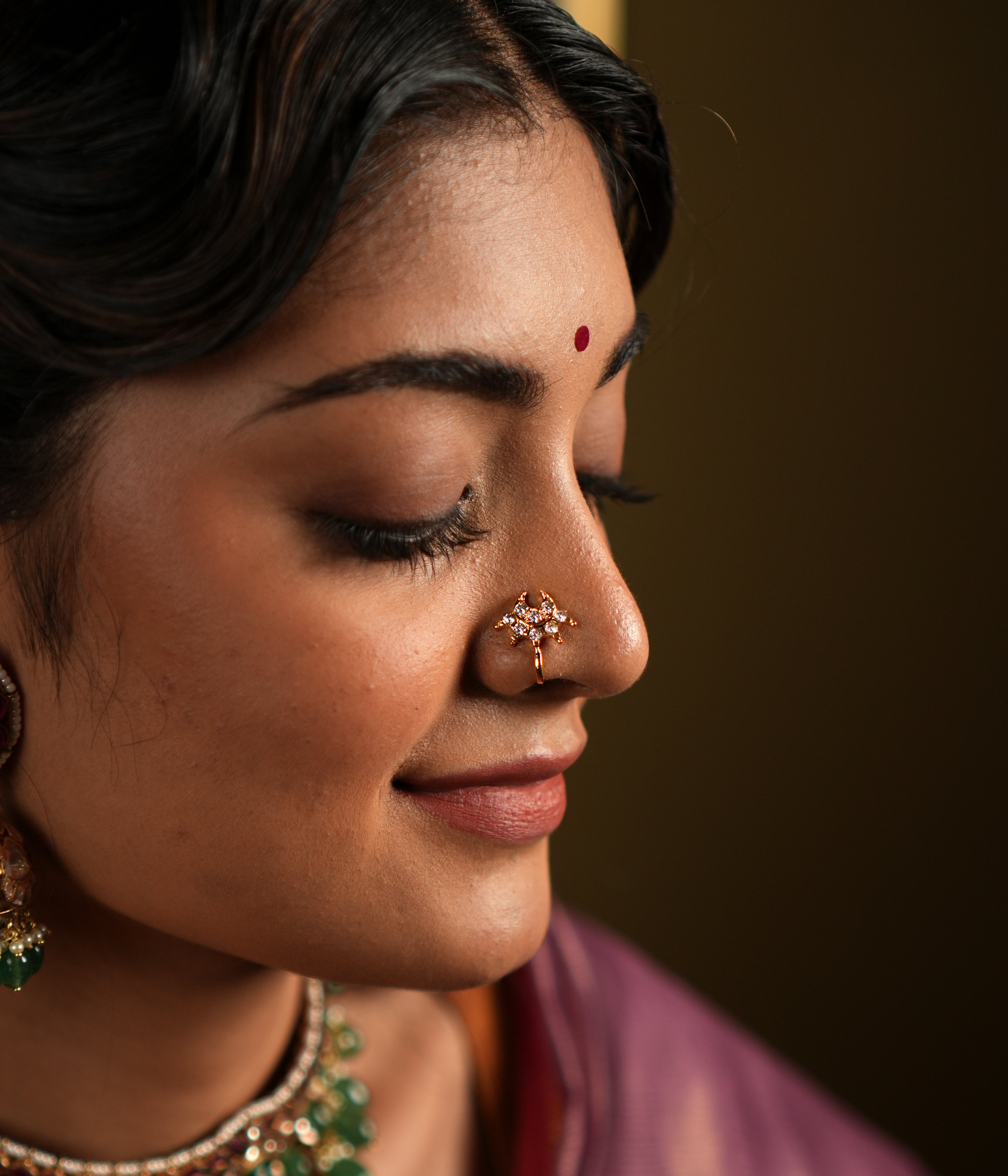 features a stunning 92.5 sterling silver nose pin with an elegant gold-plated finish. The nose pin is designed in a unique, intricate pattern adorned with sparkling stones, offering a delicate yet eye-catching appeal. Its refined craftsmanship and graceful design make it a versatile accessory, perfect for traditional attire or festive occasions.