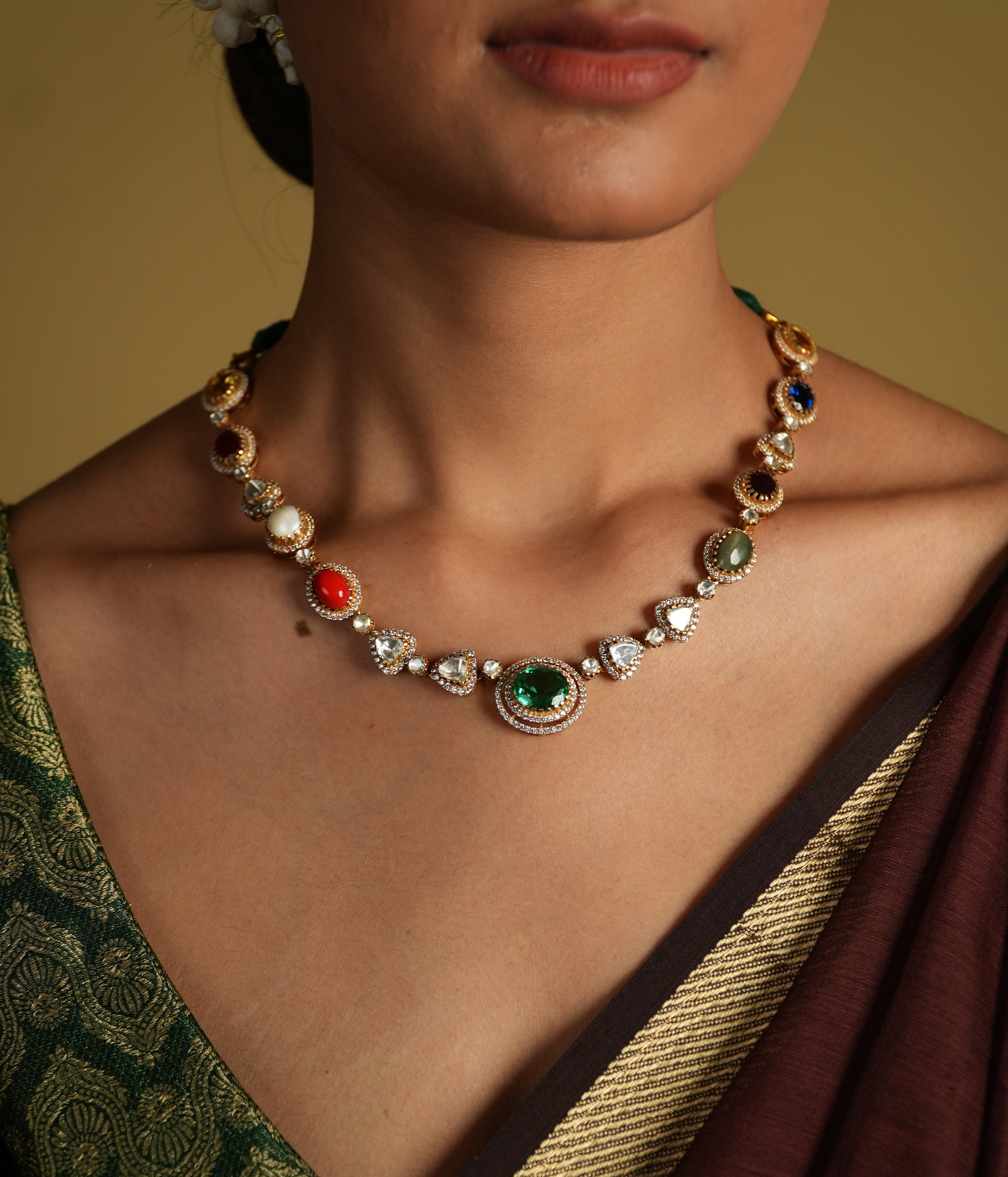 This elegant 92.5 sterling silver necklace is beautifully gold-plated and features a classic Navratna design. Adorned with nine vibrant gemstones, including emerald, ruby, sapphire, coral, and more, each stone represents celestial significance and brings a pop of color to your ensemble