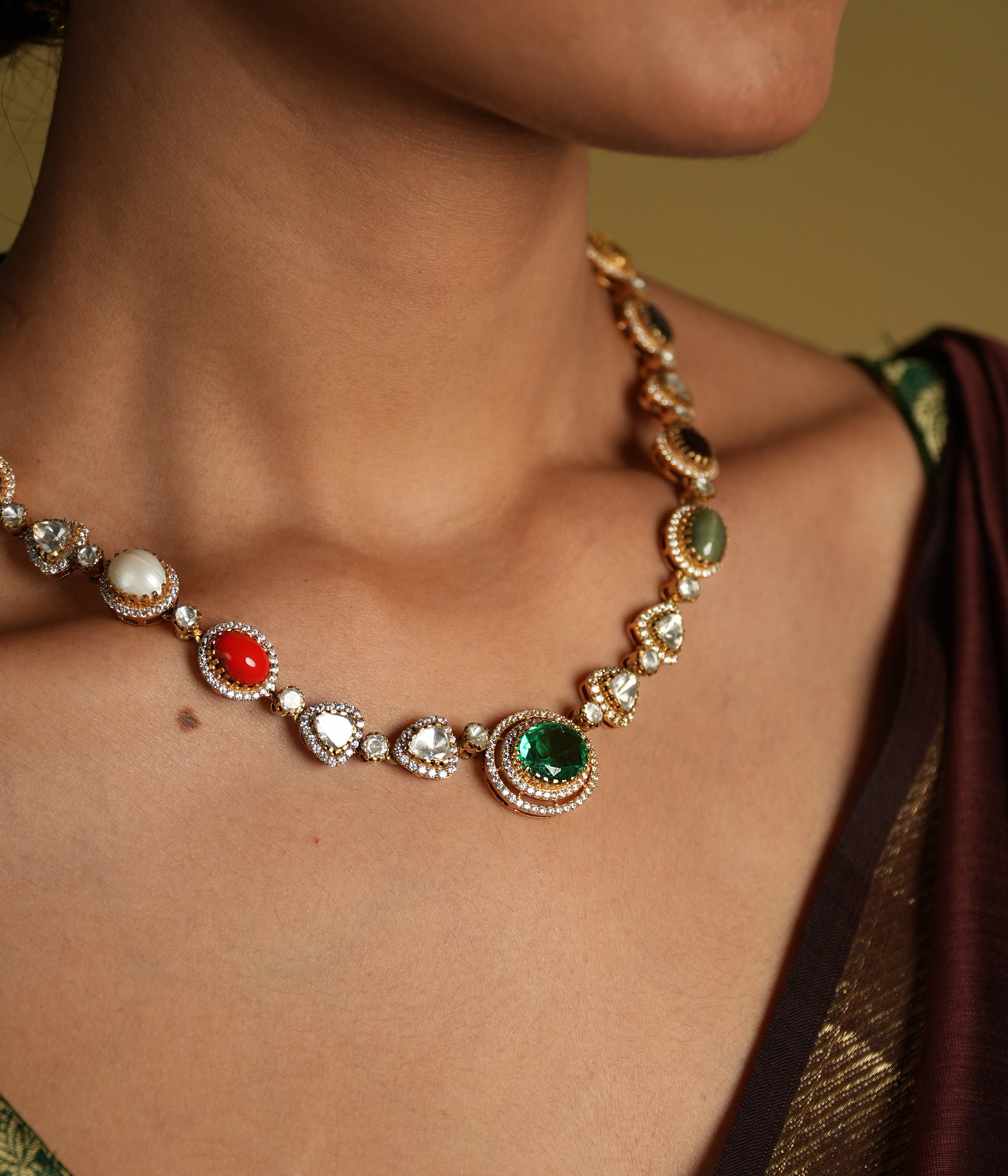 This elegant 92.5 sterling silver necklace is beautifully gold-plated and features a classic Navratna design. Adorned with nine vibrant gemstones, including emerald, ruby, sapphire, coral, and more, each stone represents celestial significance and brings a pop of color to your ensemble