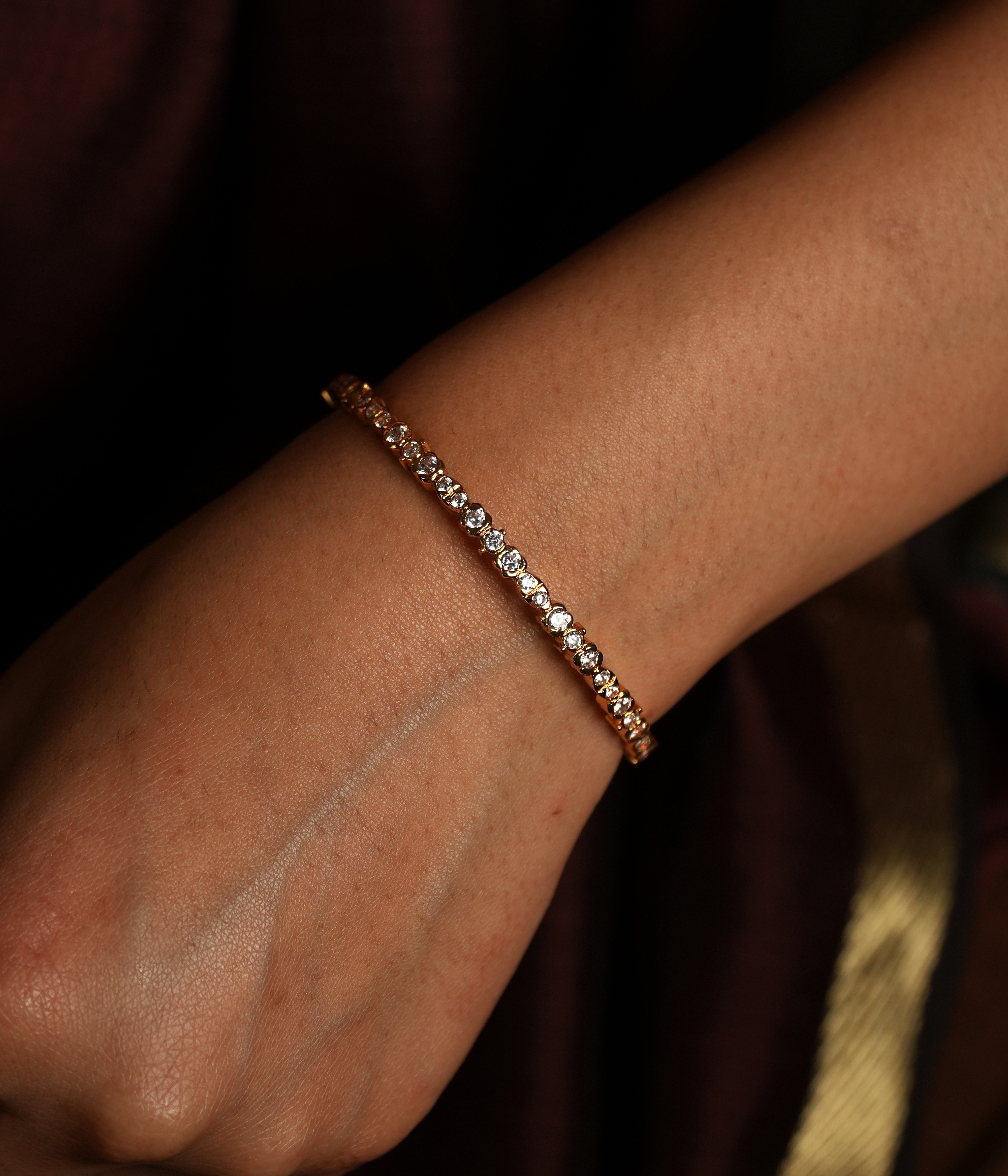 This is a close-up image of a wrist adorned with a delicate gold bracelet encrusted with swarovski Clean lines, delicate sparkle,
and heritage-inspired setting evoke the refined beauty of Tamil Nadu's iconic jewellery.
