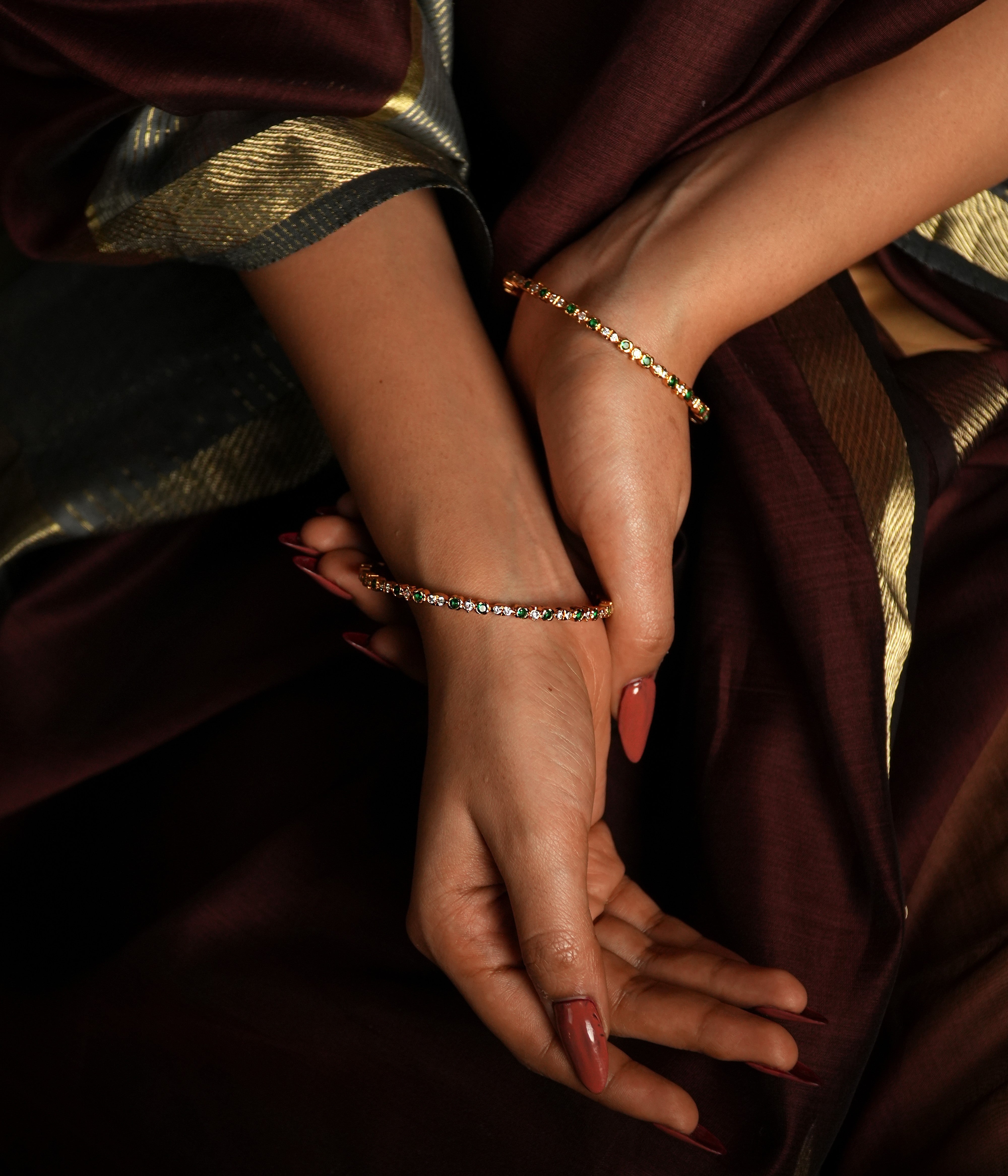 This exquisite bangle is crafted from high-quality 925 sterling silver and beautifully gold-plated for a luxurious finish. The design features delicate circular motifs, each set with shimmering stones that enhance its subtle elegance. Accented with green gemstones, it draws inspiration from the lush landscapes of Tamil Nadu, offering a whimsical touch to its refined aesthetic.