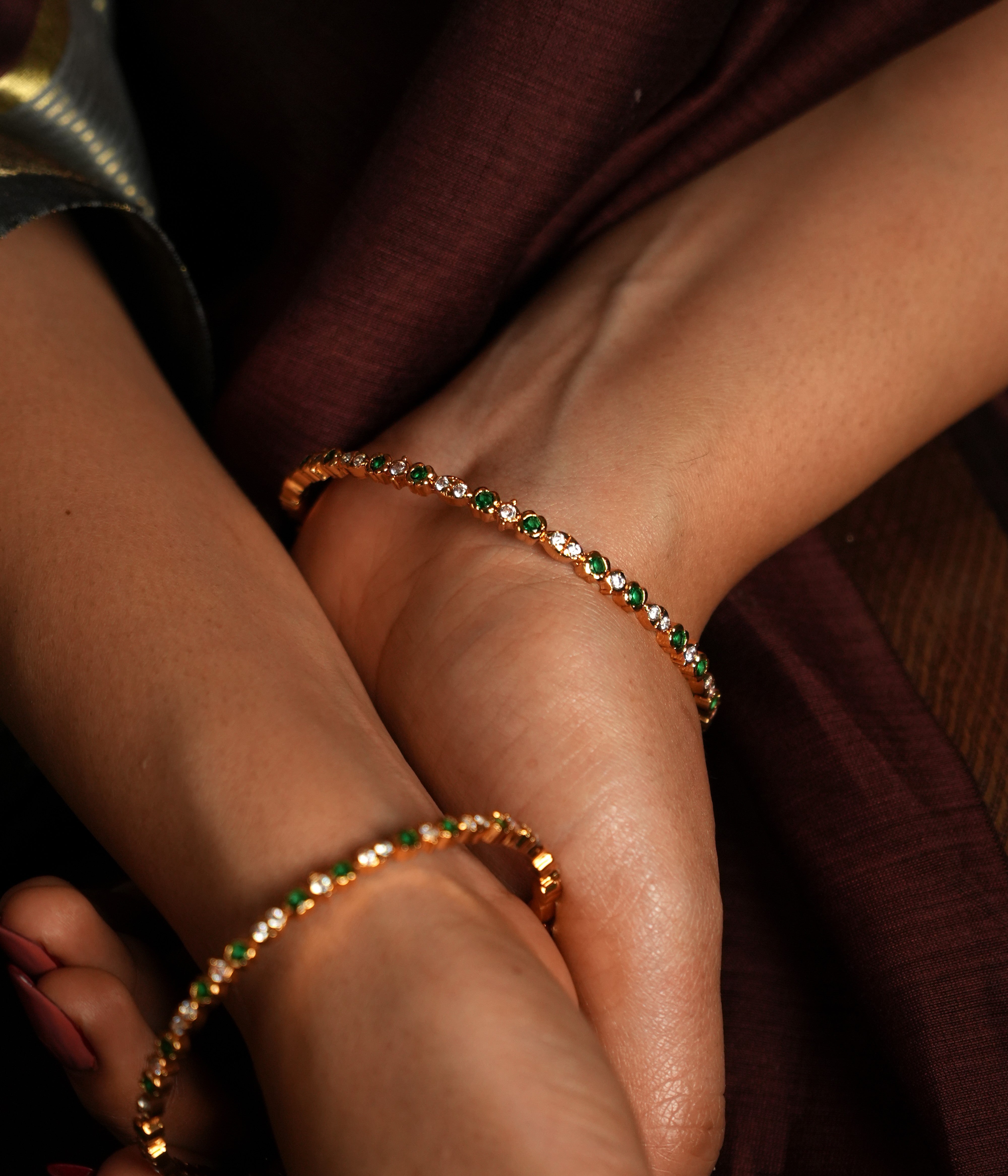 This exquisite bangle is crafted from high-quality 925 sterling silver and beautifully gold-plated for a luxurious finish. The design features delicate circular motifs, each set with shimmering stones that enhance its subtle elegance. Accented with green gemstones, it draws inspiration from the lush landscapes of Tamil Nadu, offering a whimsical touch to its refined aesthetic.