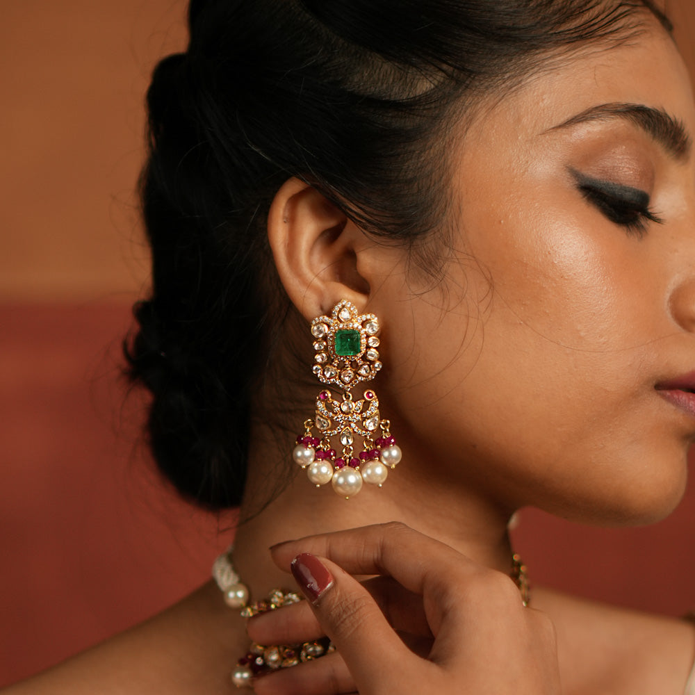 Elegant dangler earrings featuring a floral design adorned with Green Gemstone, Moissanite Polki Stones, Red Beads, Pearls, and CZ Stones. The earrings showcase a continuous arrangement of Polki and Red Beads, gracefully finished with delicate pearl drops for a sophisticated look.