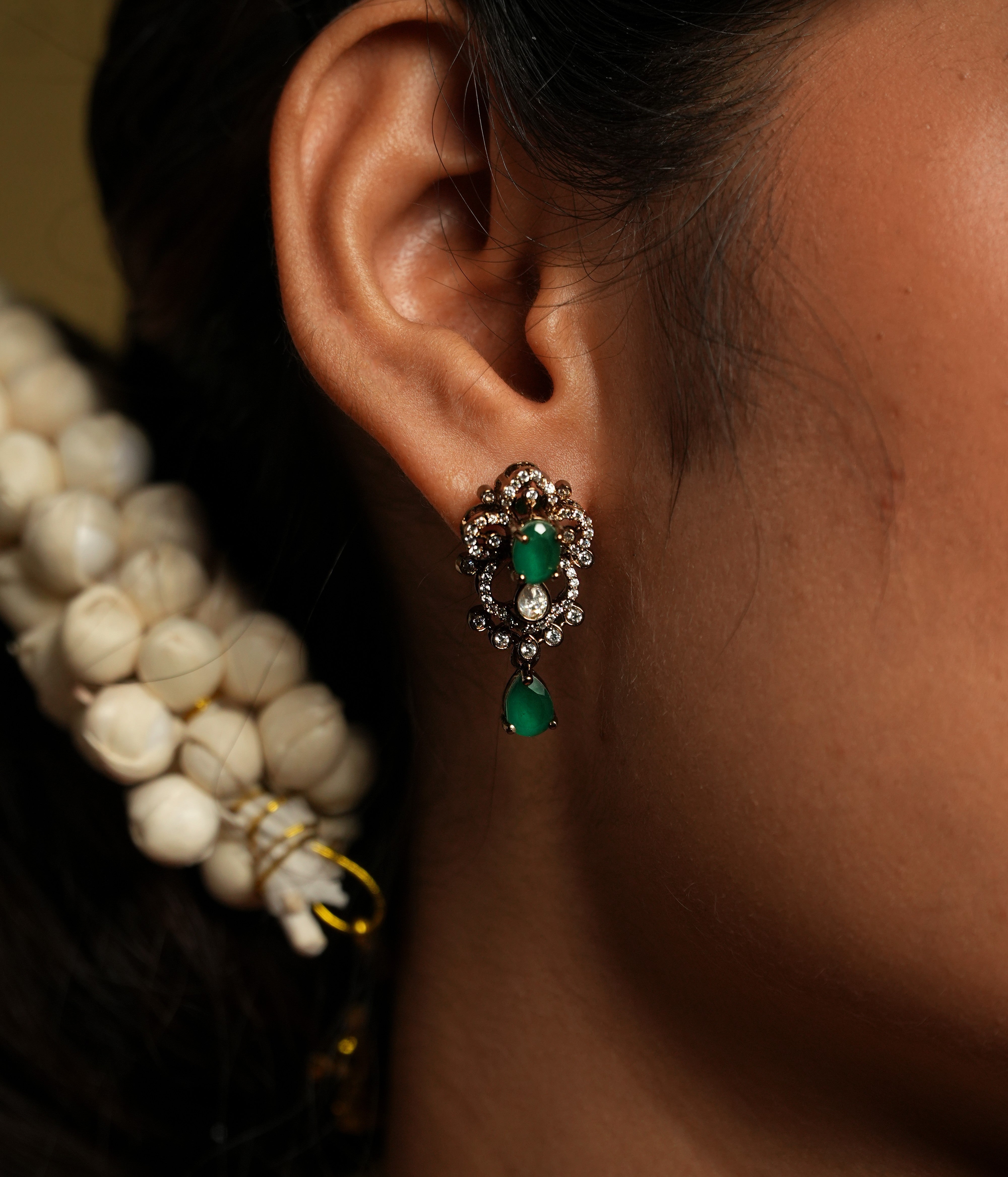 This exquisitely designed ear stud captures the essence of nature's beauty through an abstract floral motif. The fiery sparkle of moissanite is elegantly complemented by the lush, vibrant glow of a green gemstone, creating a striking visual contrast. Crafted from 925 silver and finished with gold plating, this ear stud offers a luxurious yet timeless appeal.