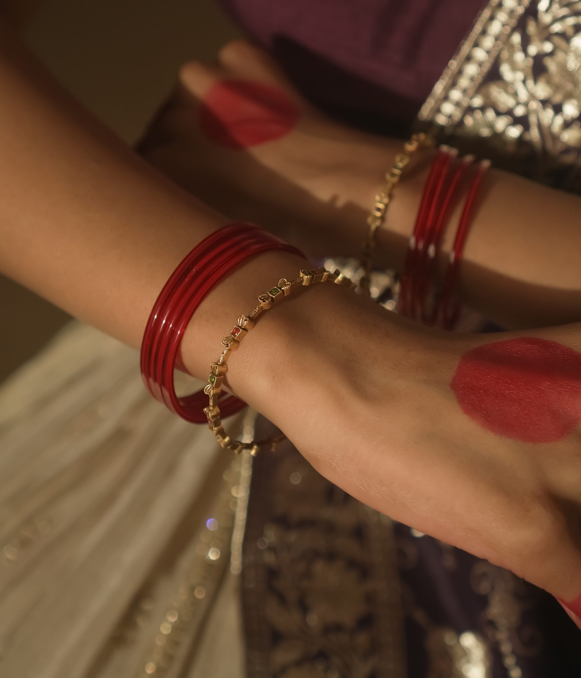 Close-up of a wrist with red and gold bracelets against a patterned fabric background