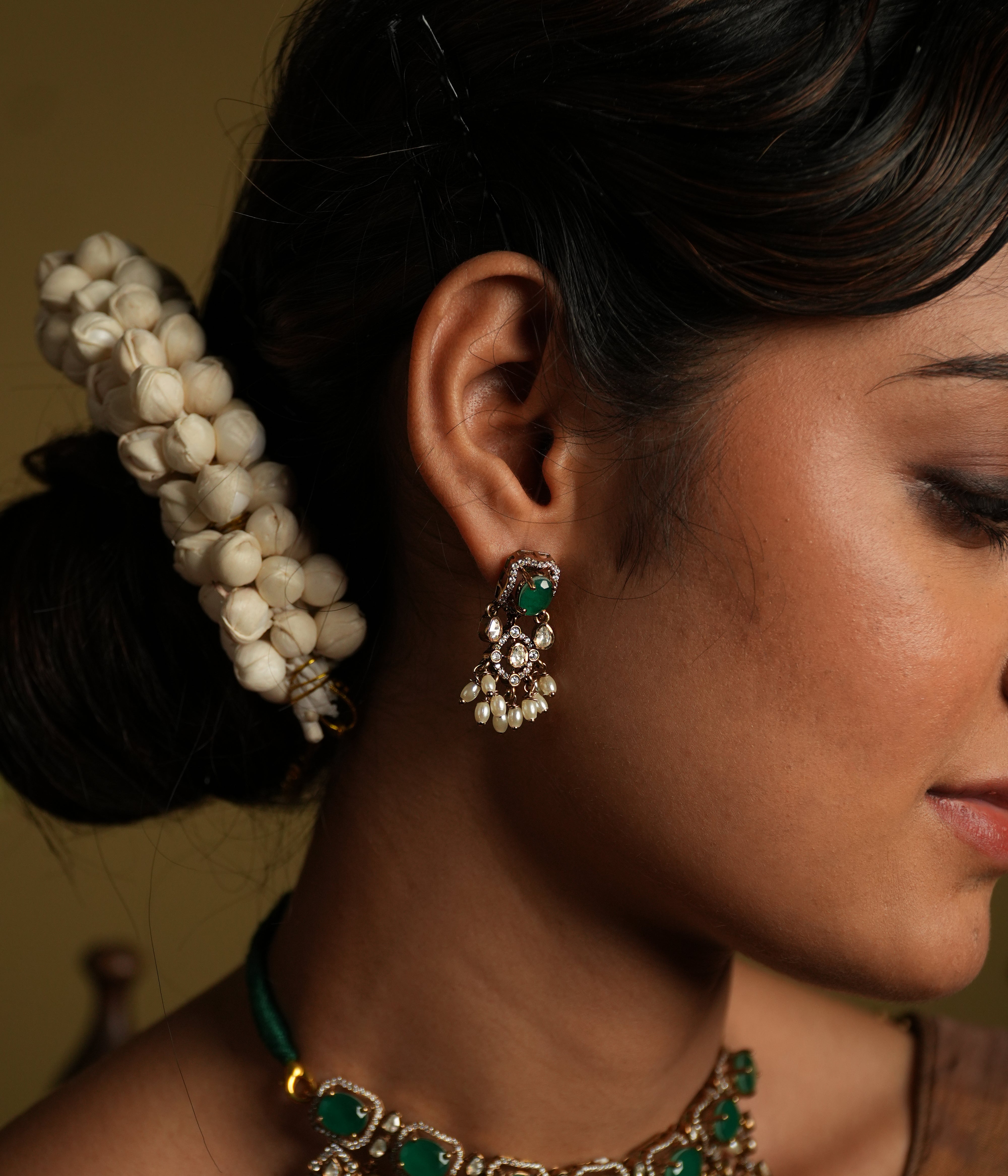 Enhance your traditional look with this exquisite silver gold-plated jewelry set featuring a stunning pair of earrings and a matching necklace. The earrings are intricately designed with green gemstones as the centerpiece, surrounded by shimmering American diamonds and delicate pearl drops for a timeless appeal.