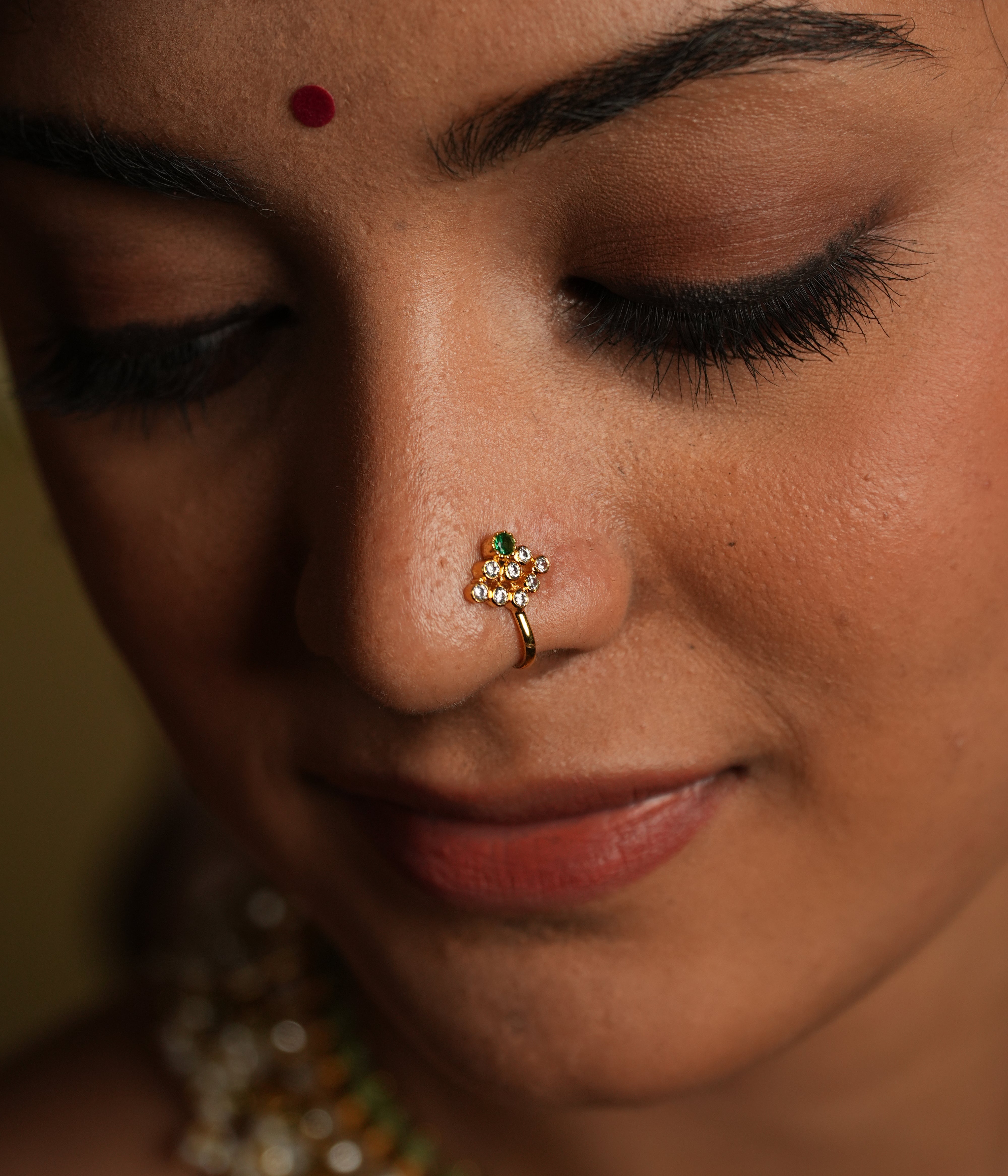 Embrace timeless beauty with this delicate floral nose pin, adorned with moissanite stones and a touch of green gemstone detailing. Crafted in silver with gold plating, this elegant piece is designed to add a subtle sparkle to your look. The intricate floral design enhances its charm, making it a perfect blend of tradition and modern sophistication.