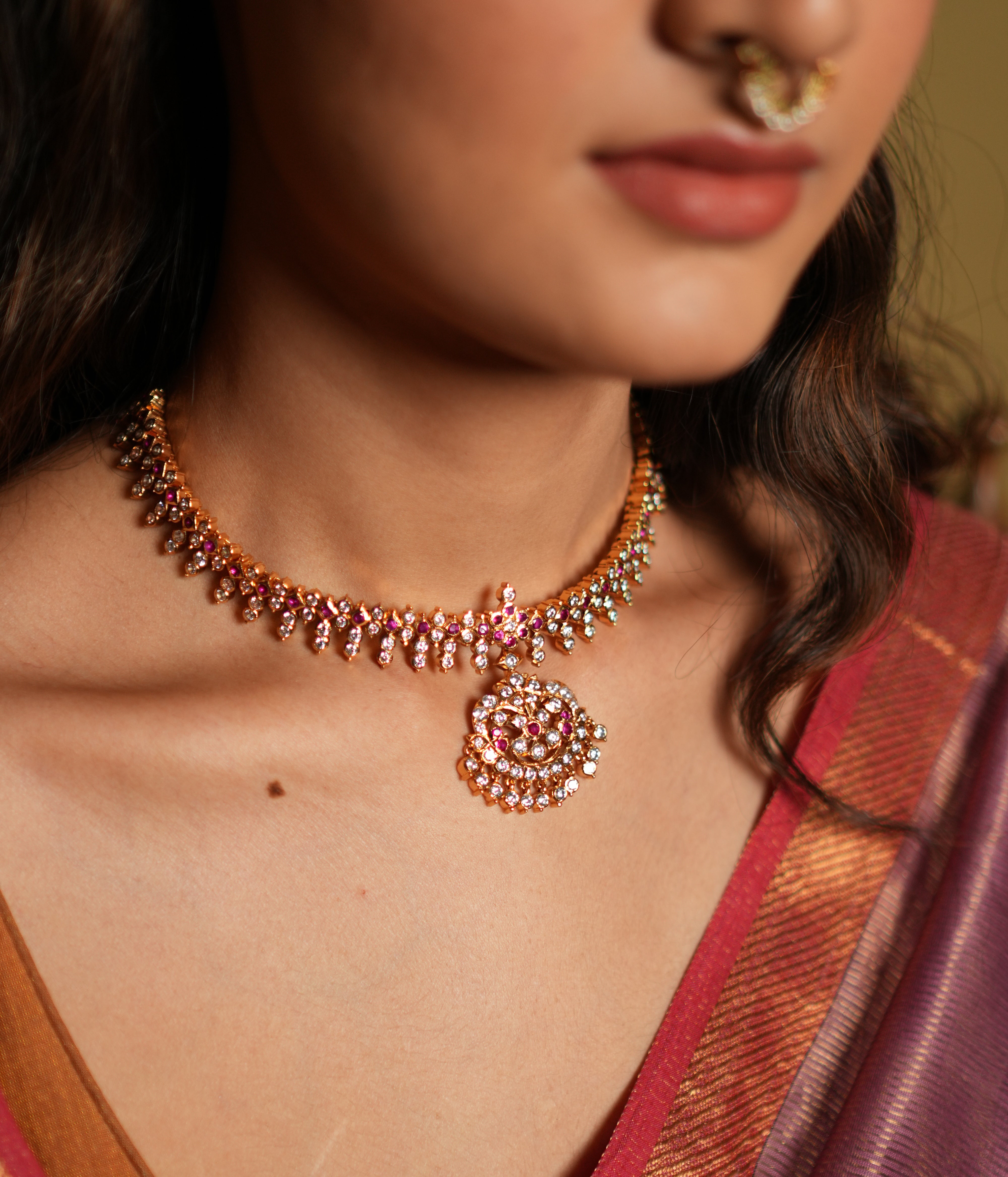 Elevate your traditional attire with this exquisite Attigai necklace, crafted from 92.5 sterling silver and finished with a rich 22-carat gold plating. Adorned with dazzling Swarovski crystals and accented with vivid pink gemstones, this necklace exudes timeless elegance and sophistication. 